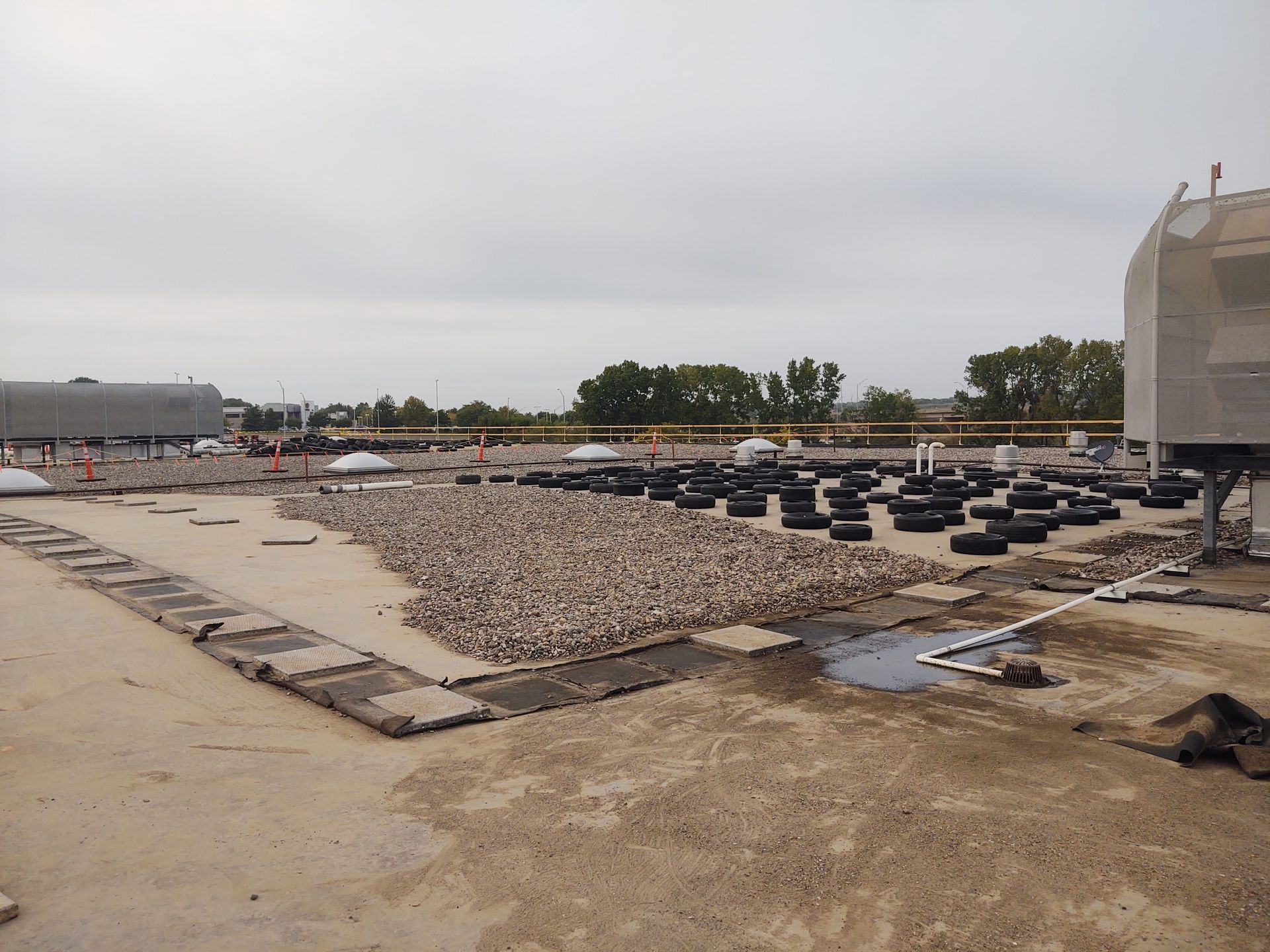 An industrial flat roof featuring a section of loose gravel, rows of black rubber tires, and exposed concrete under a sky.
