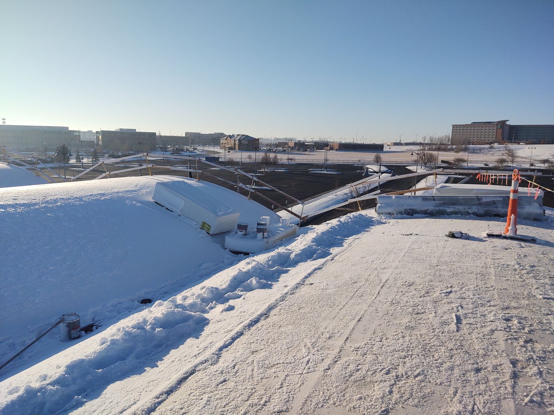 A snow-covered construction site with large mounds of snow and concrete barriers under a clear blue sky.