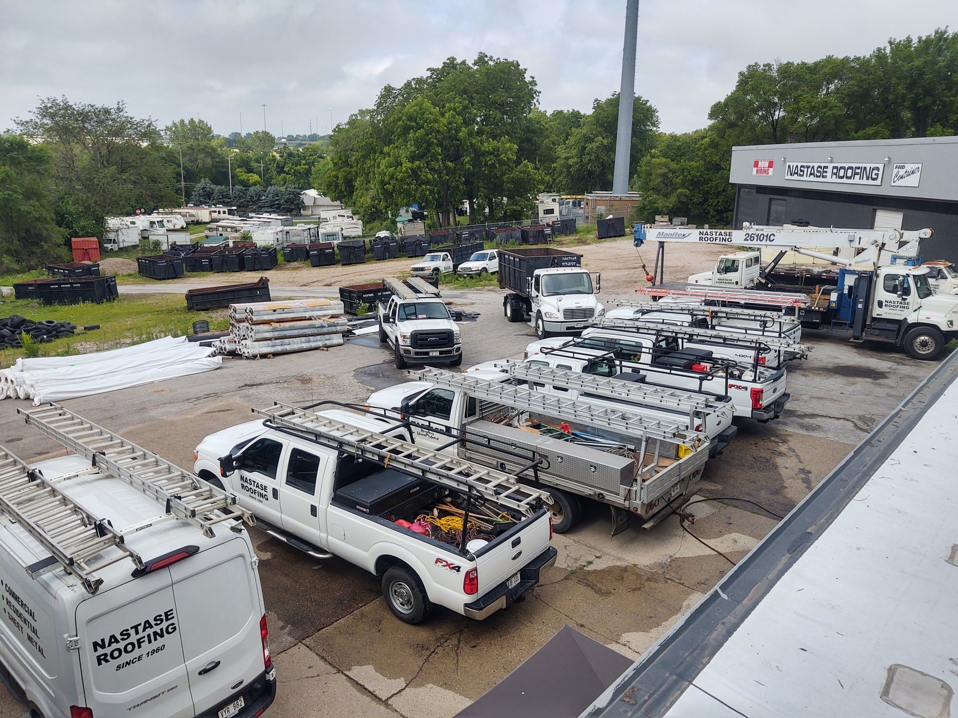 An aerial view of a maintenance yard with white service trucks, utility vans, equipment, and parked trailers.