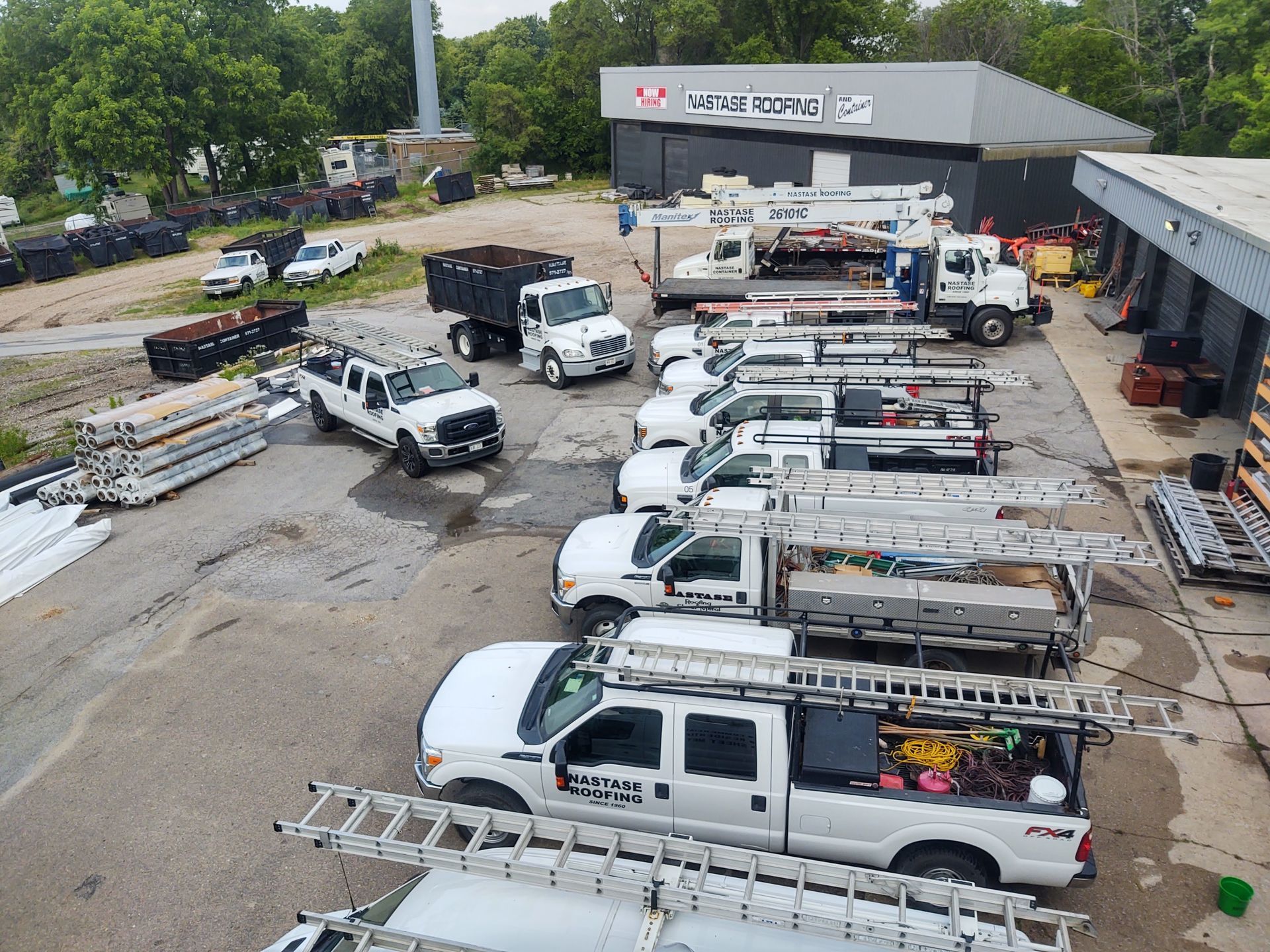 High-angle view of a utility company yard with several white service trucks equipped with roof-mounted ladders.