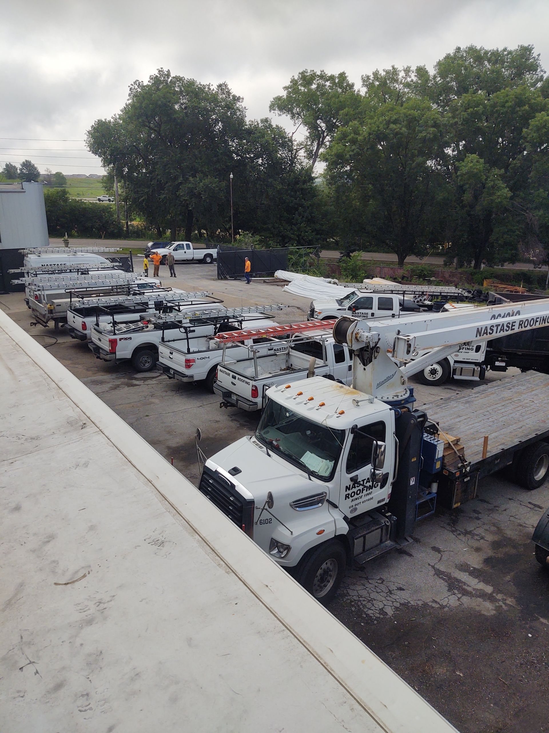 A row of white utility trucks parked in an outdoor gravel lot under an overcast sky.