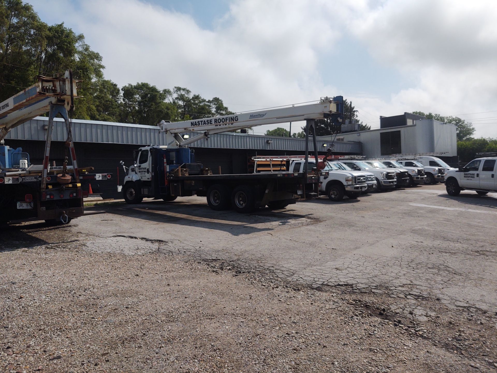Several utility and pickup trucks are parked in a gravel lot in front of a long, single-story industrial building.