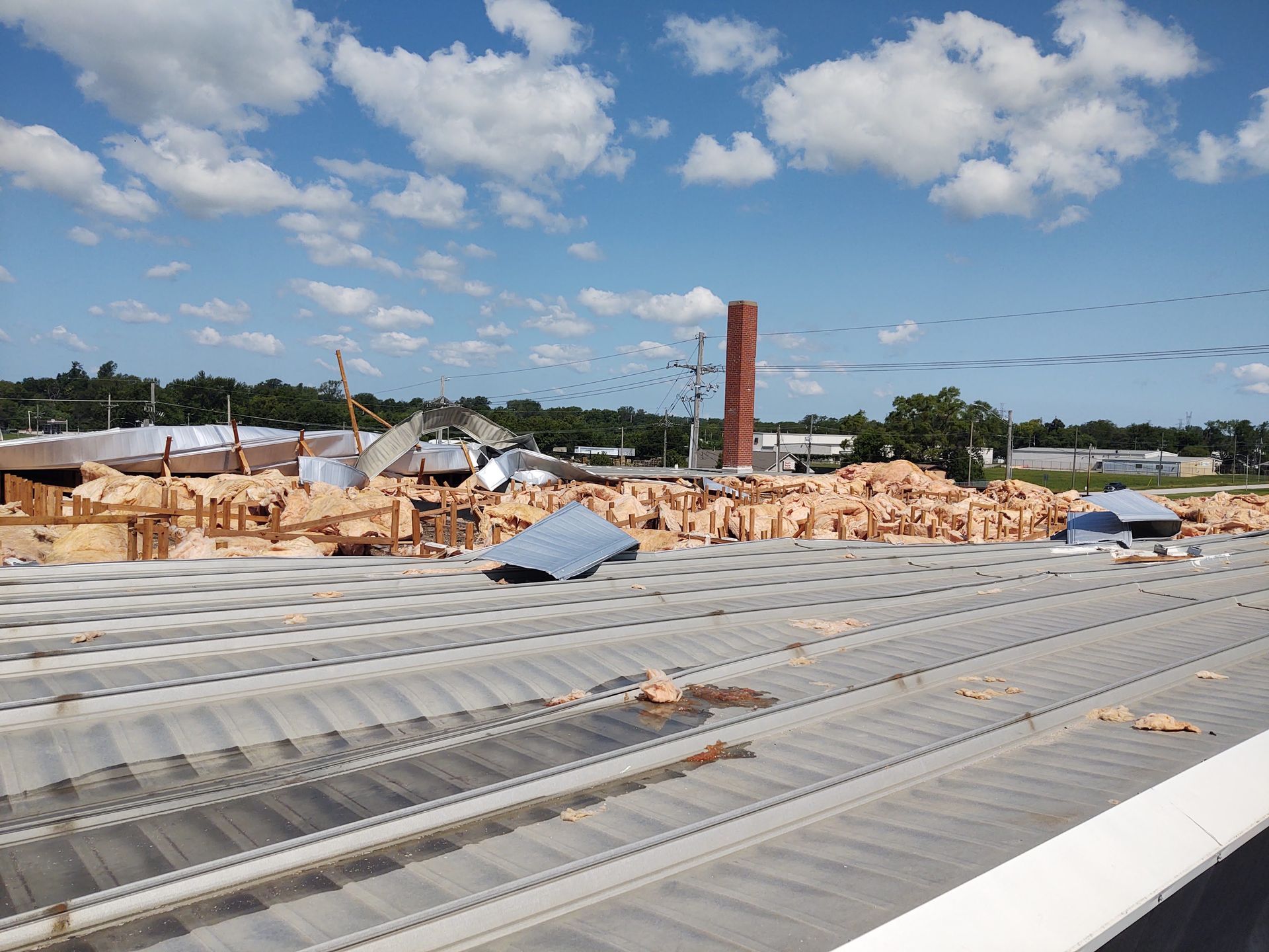 Debris and ruins of a damaged building under a blue sky with scattered clouds and a tall, lone brick chimney standing.