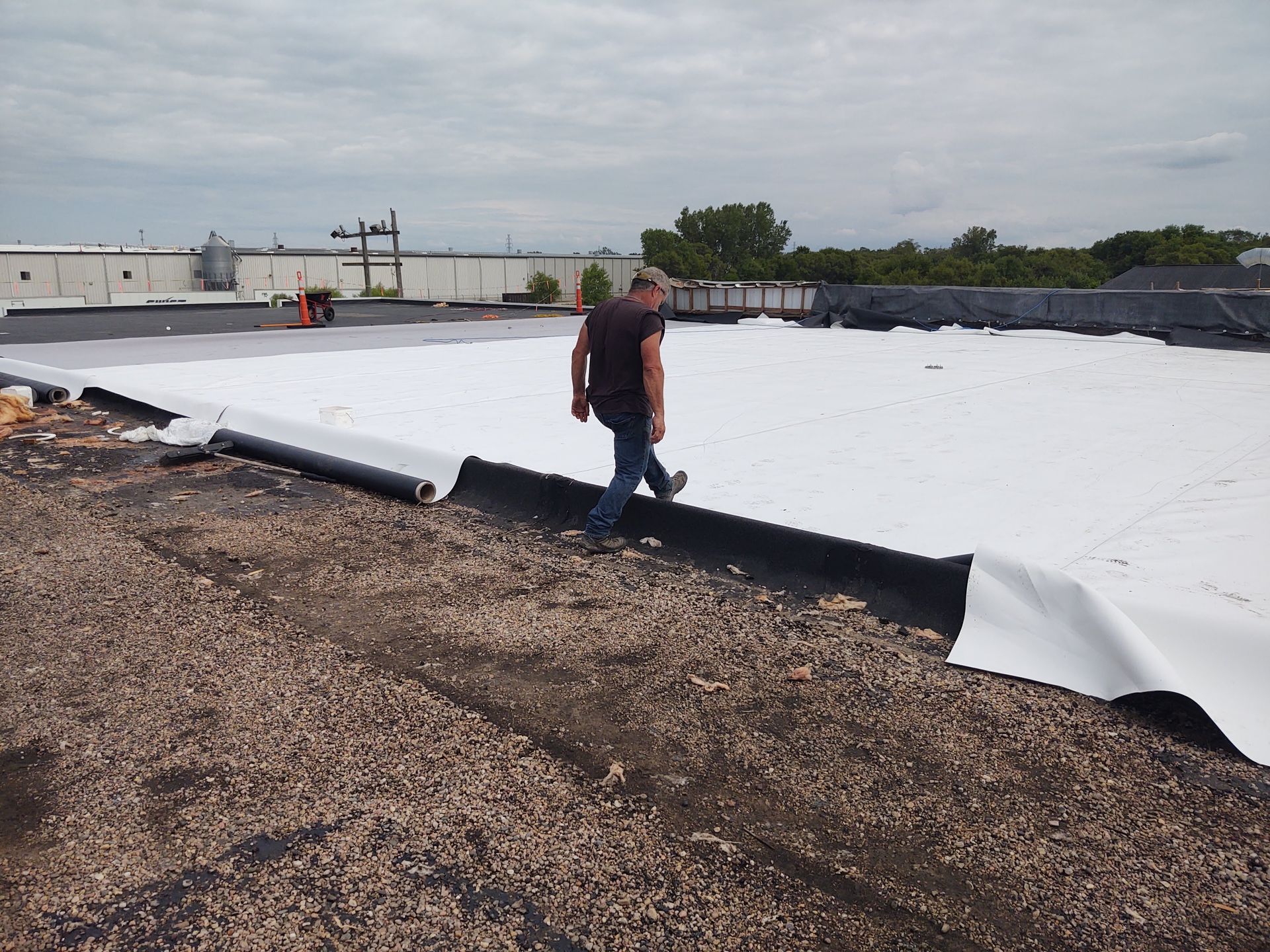 A person walks across a white TPO roofing membrane being installed over an existing gravel roof on a commercial building.