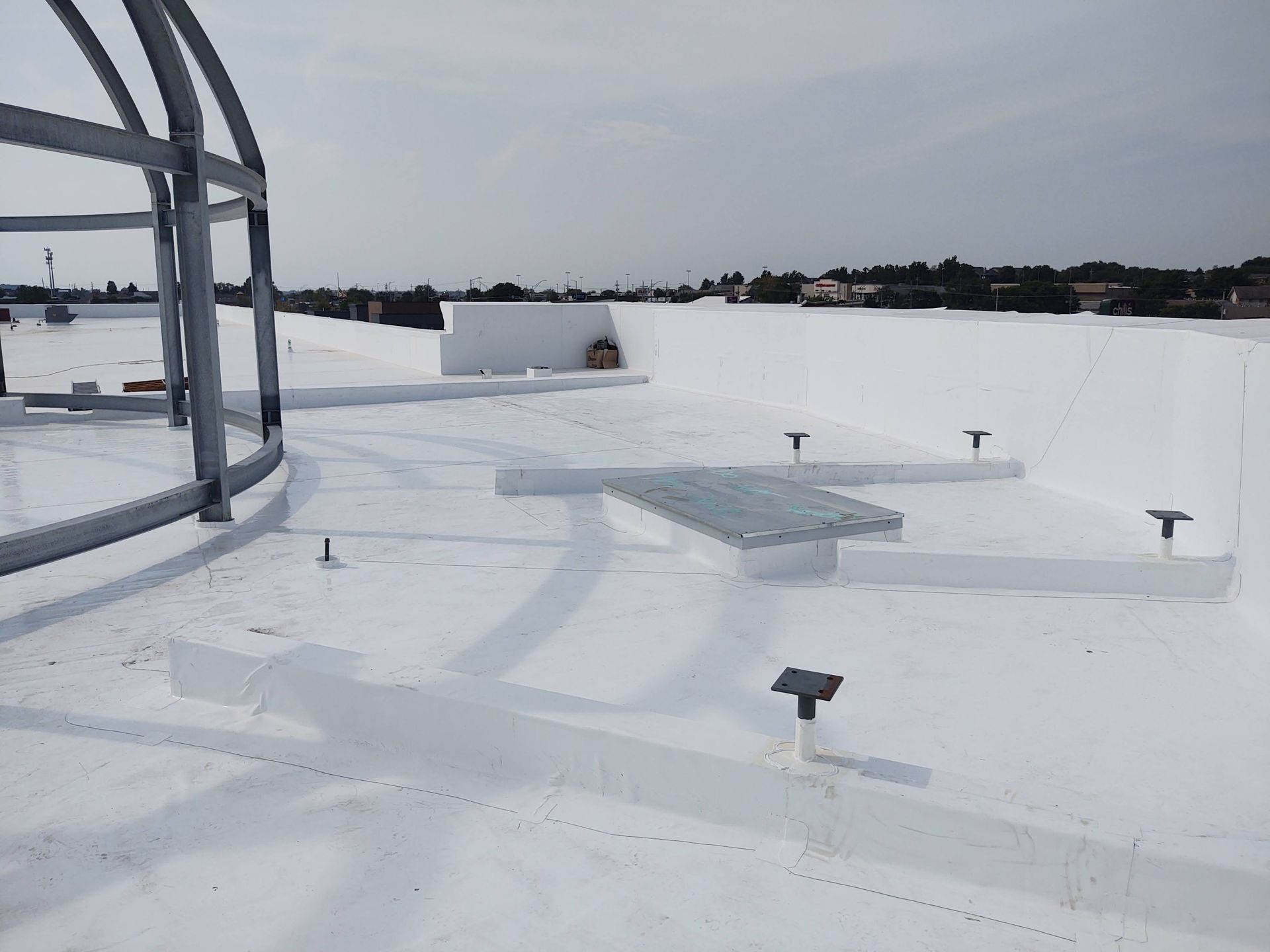 A white-coated flat roof featuring a metal dome frame, a small walkway, and several small support posts.