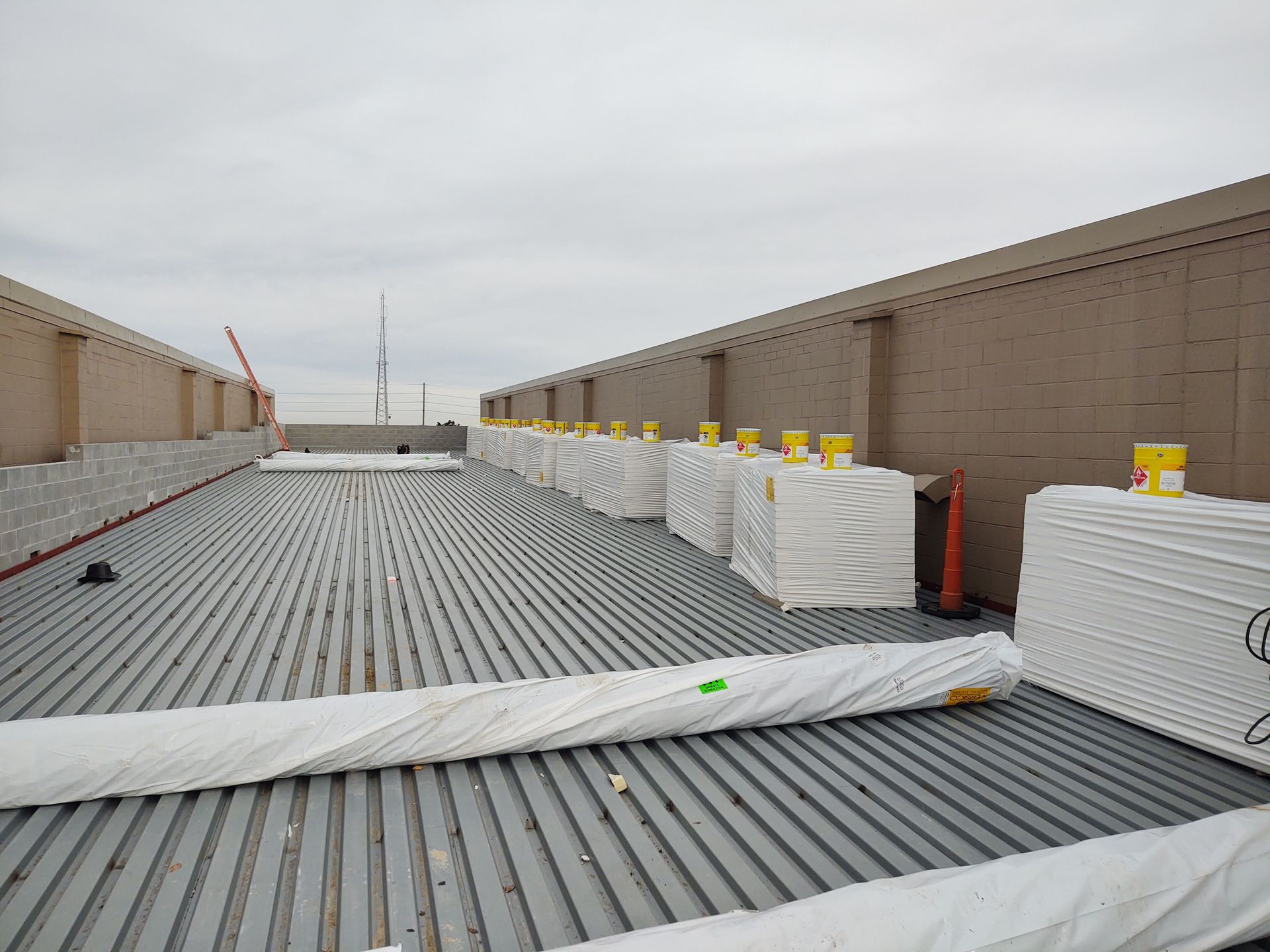 Rows of stacked white insulation bundles sit on a corrugated metal rooftop under a cloudy sky.
