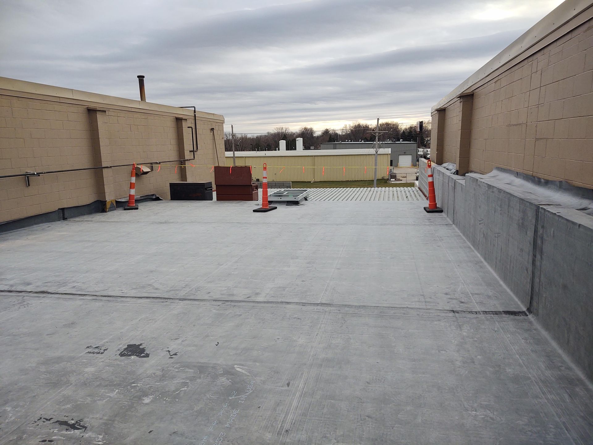 A flat, grey roof section framed by light-colored masonry walls, with orange traffic cones placed along the perimeter.