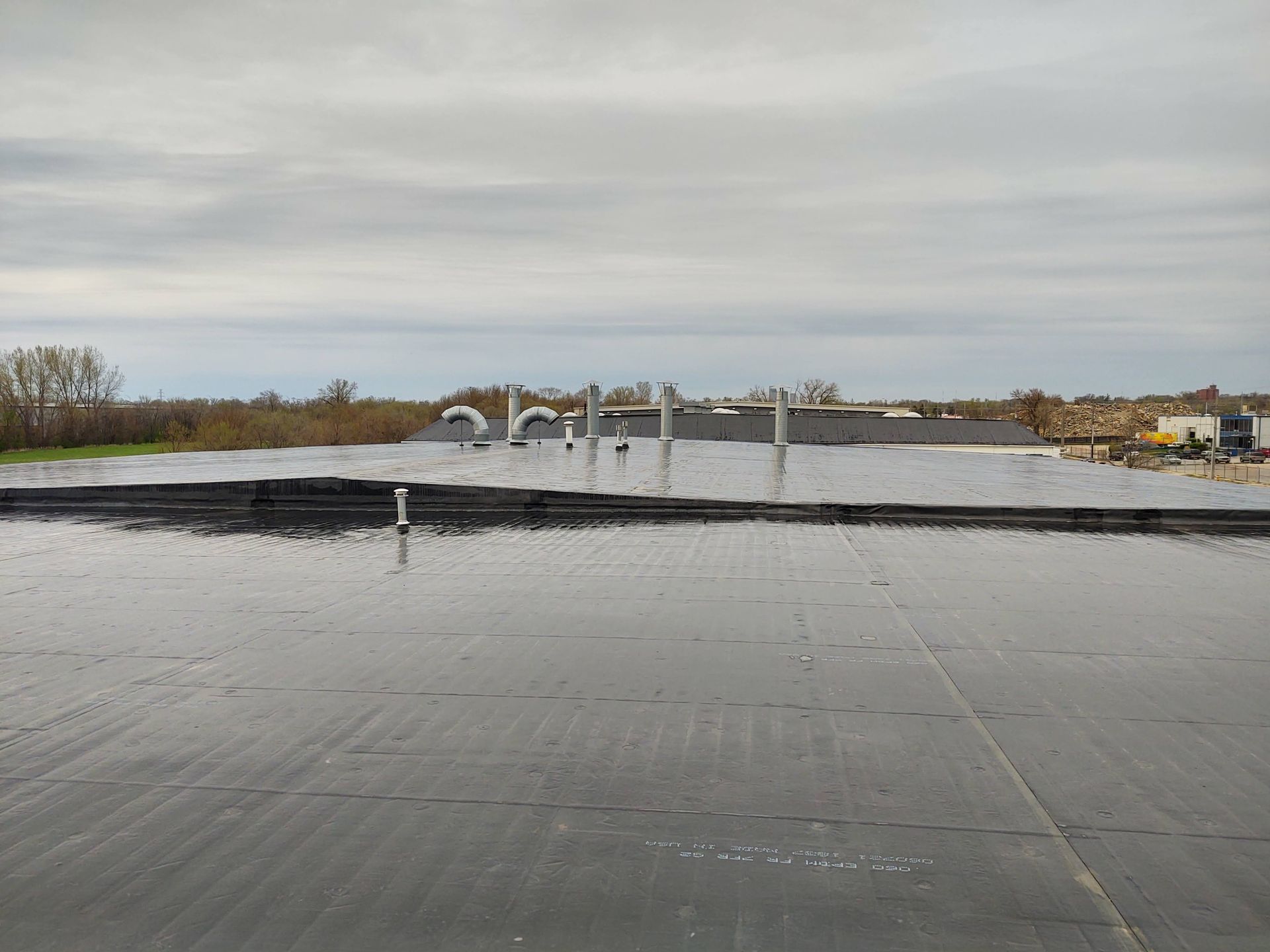 A wide, flat black rubber roof surface under a cloudy sky, with several ventilation pipes rising from the rear.