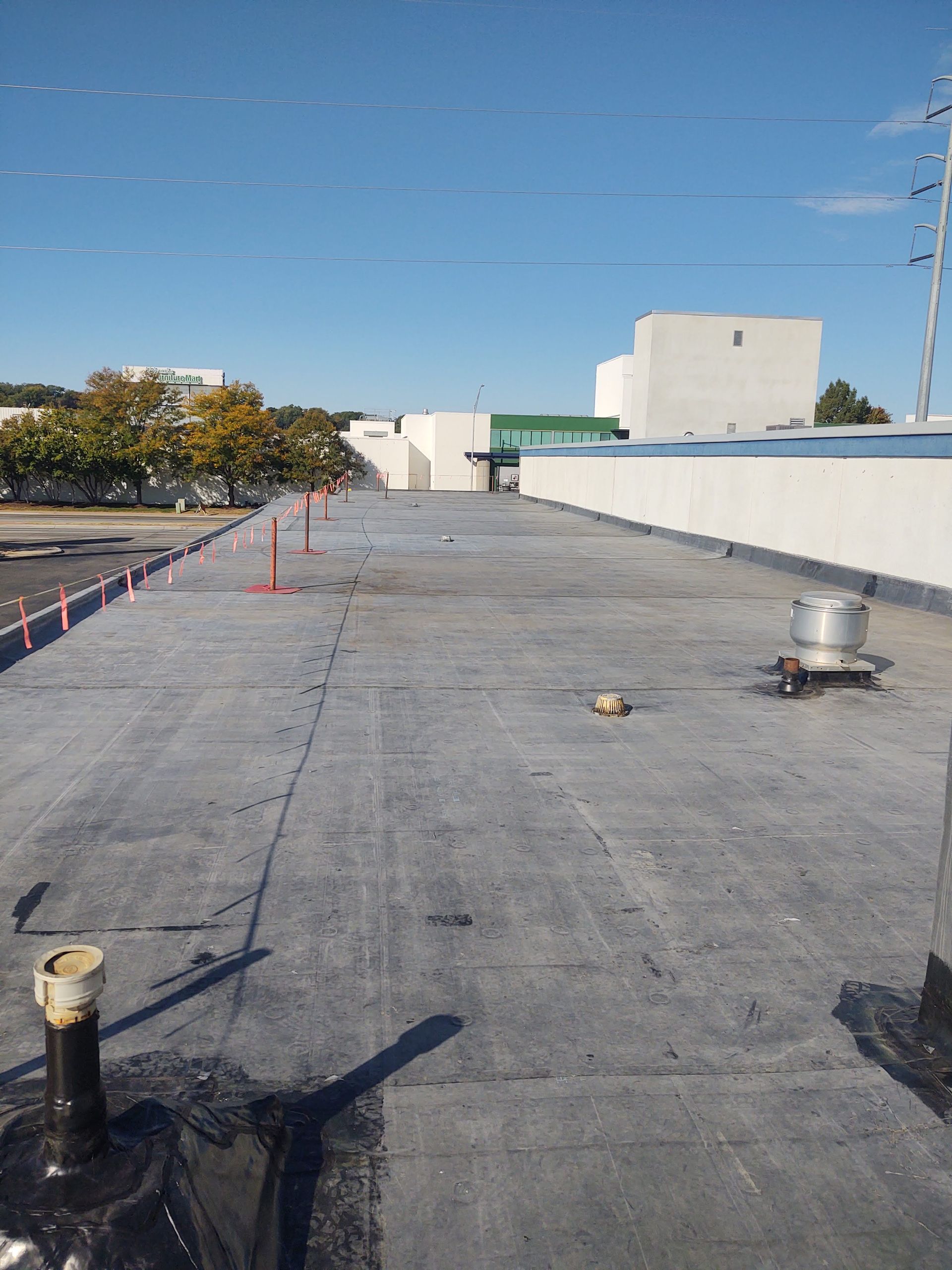 A flat commercial roof with grey membrane, a vent, a mechanical exhaust fan, and orange safety markers in the distance.