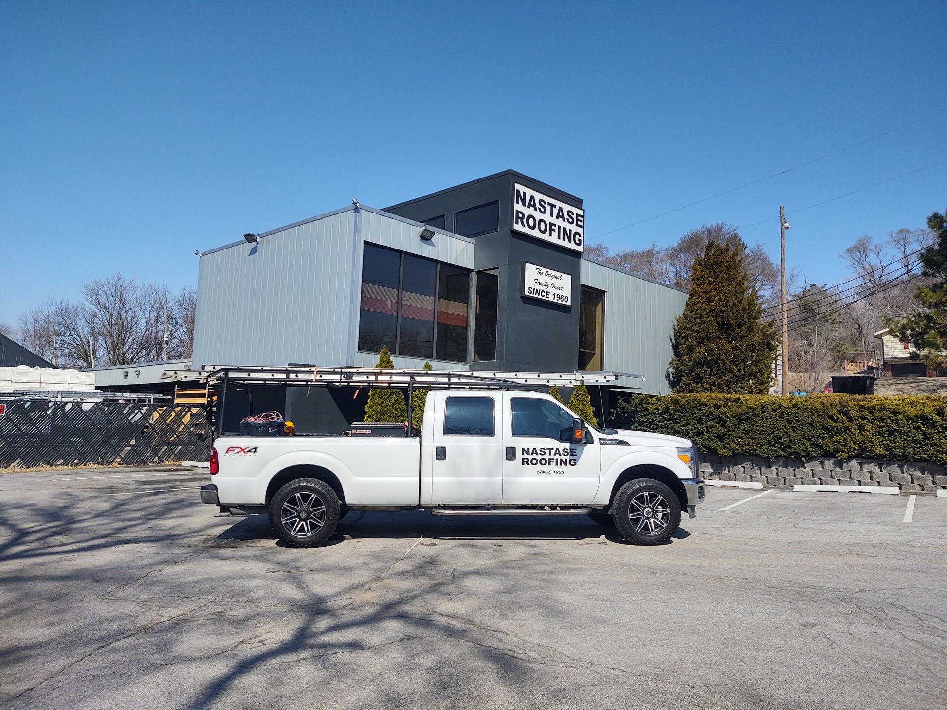 A white Mastas Roofing pickup truck is parked in a gravel lot in front of a gray metal commercial building.