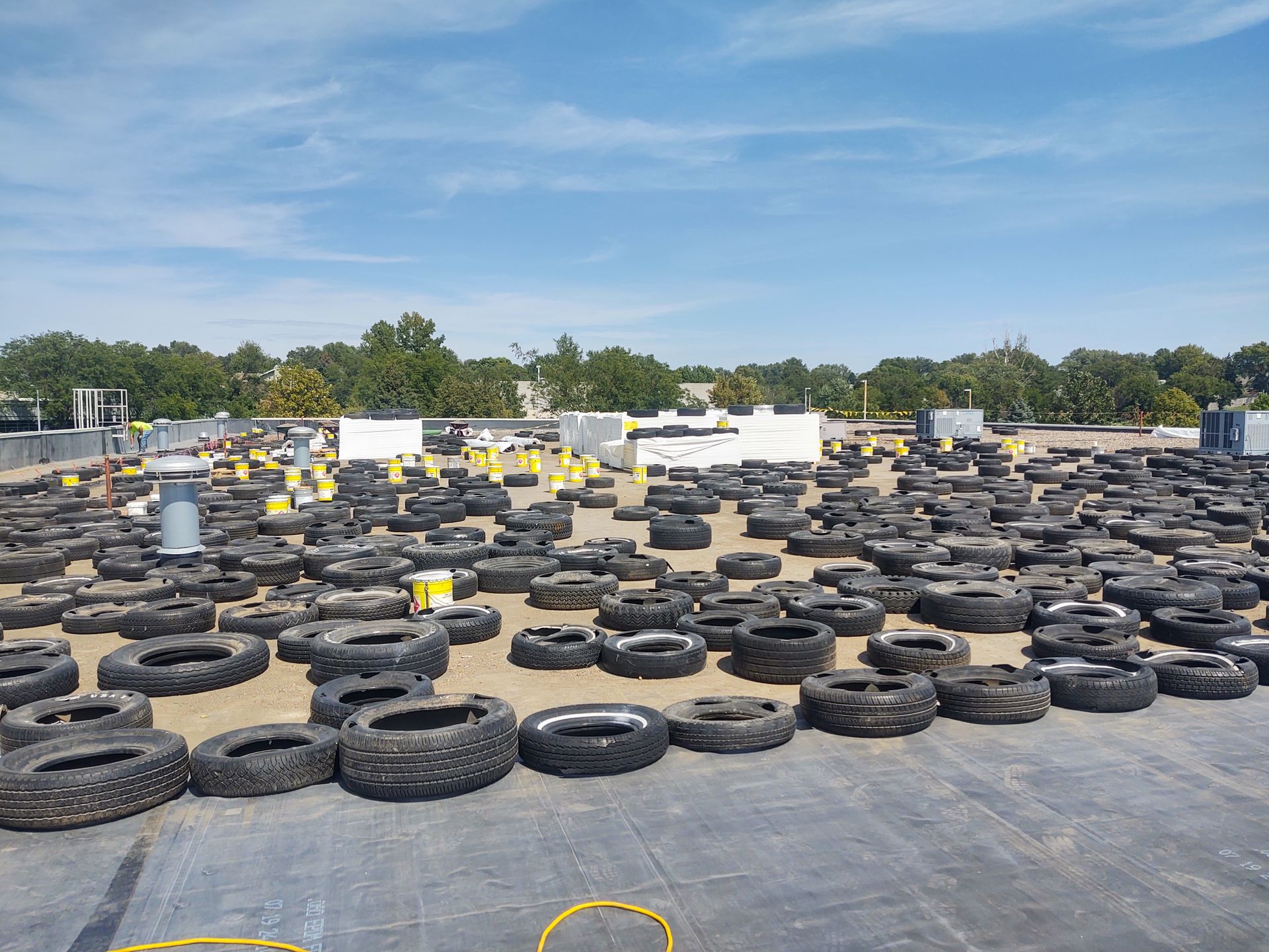 A flat, gravel-covered roof is densely covered with hundreds of scattered black rubber tires under a clear blue sky.