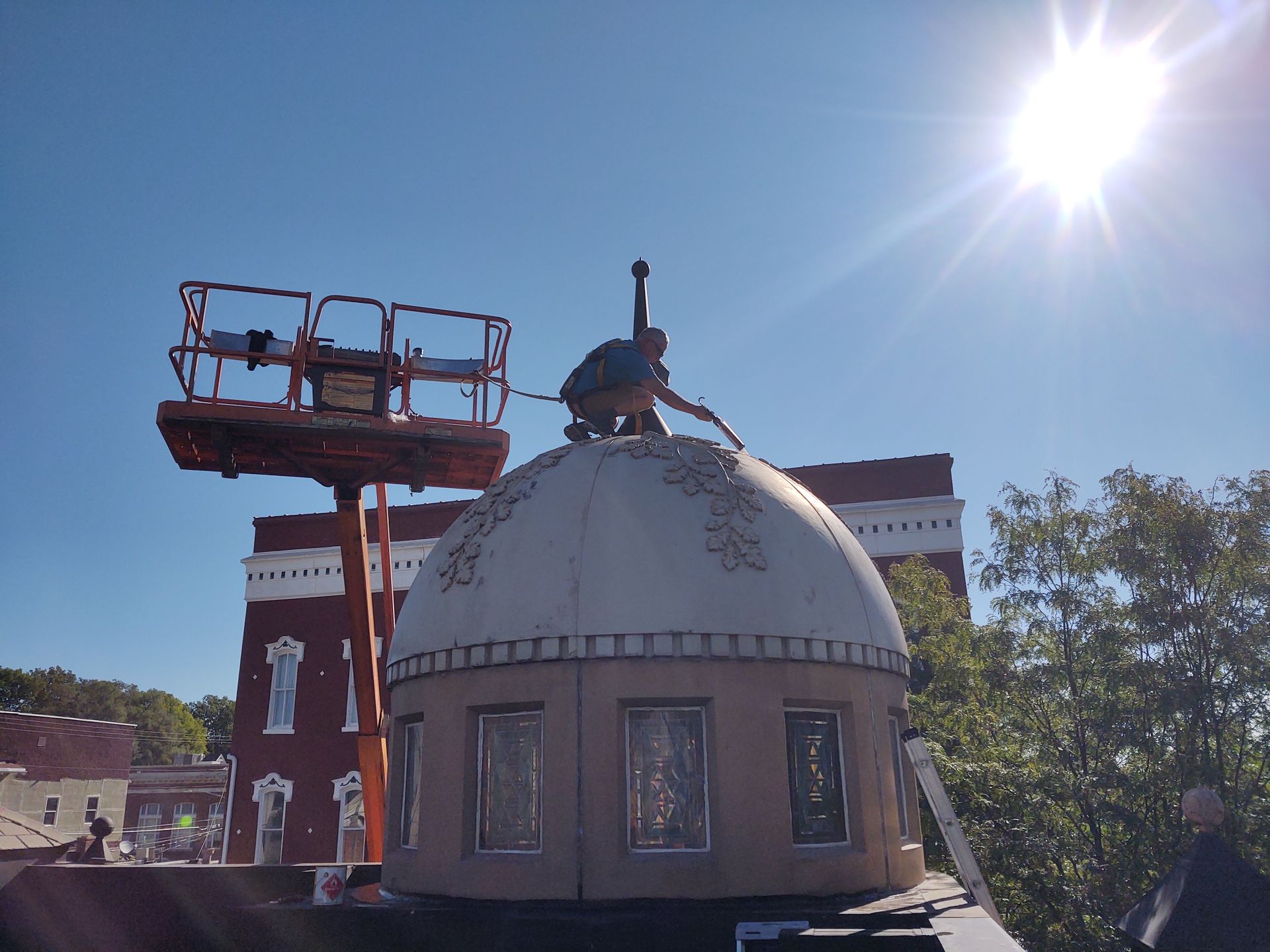 A person stands on a dome structure, working near a cherry picker lift on a sunny day with blue sky.