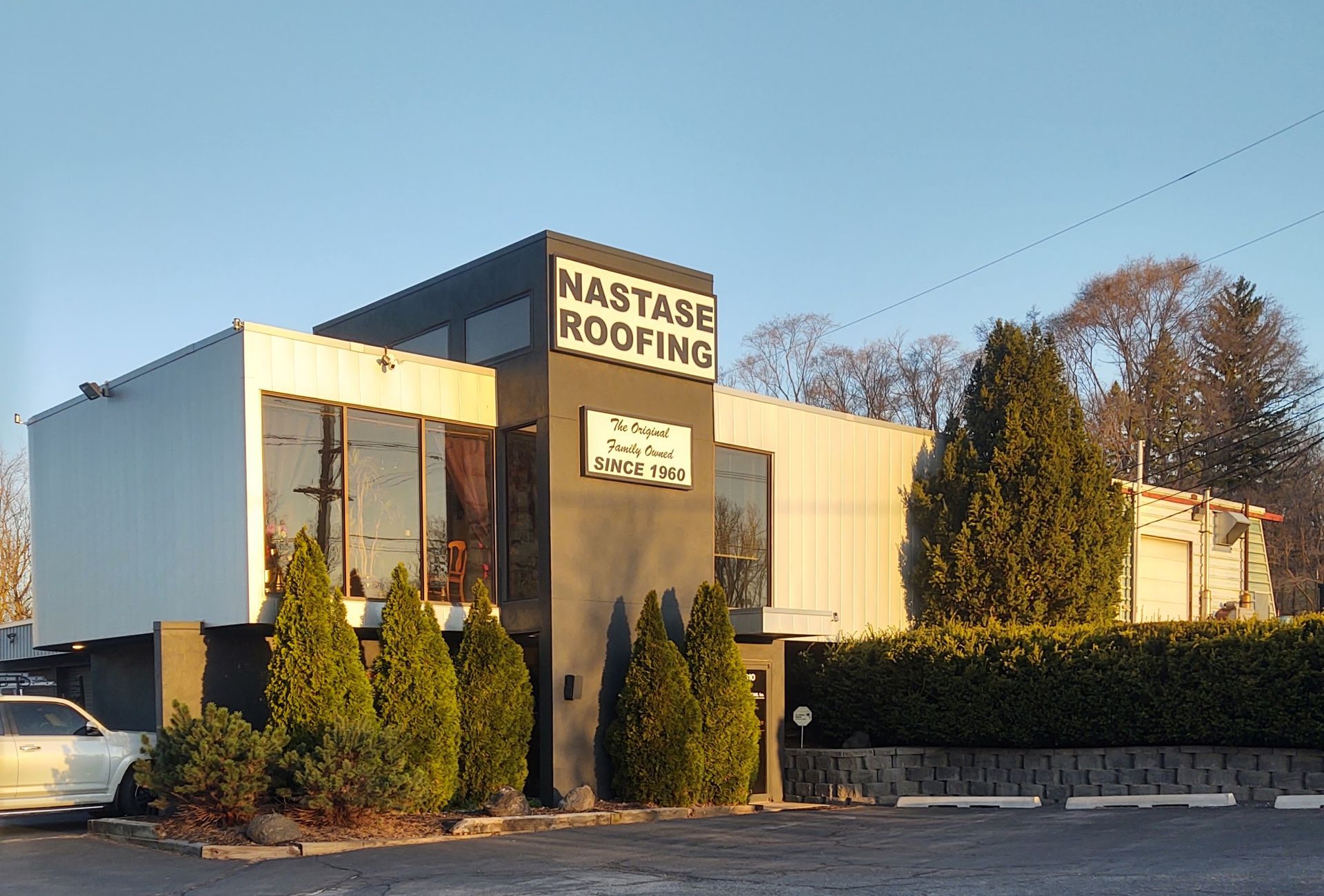 A two-story commercial building for Nastase Roofing featuring a gray facade, large windows, and manicured landscaping.
