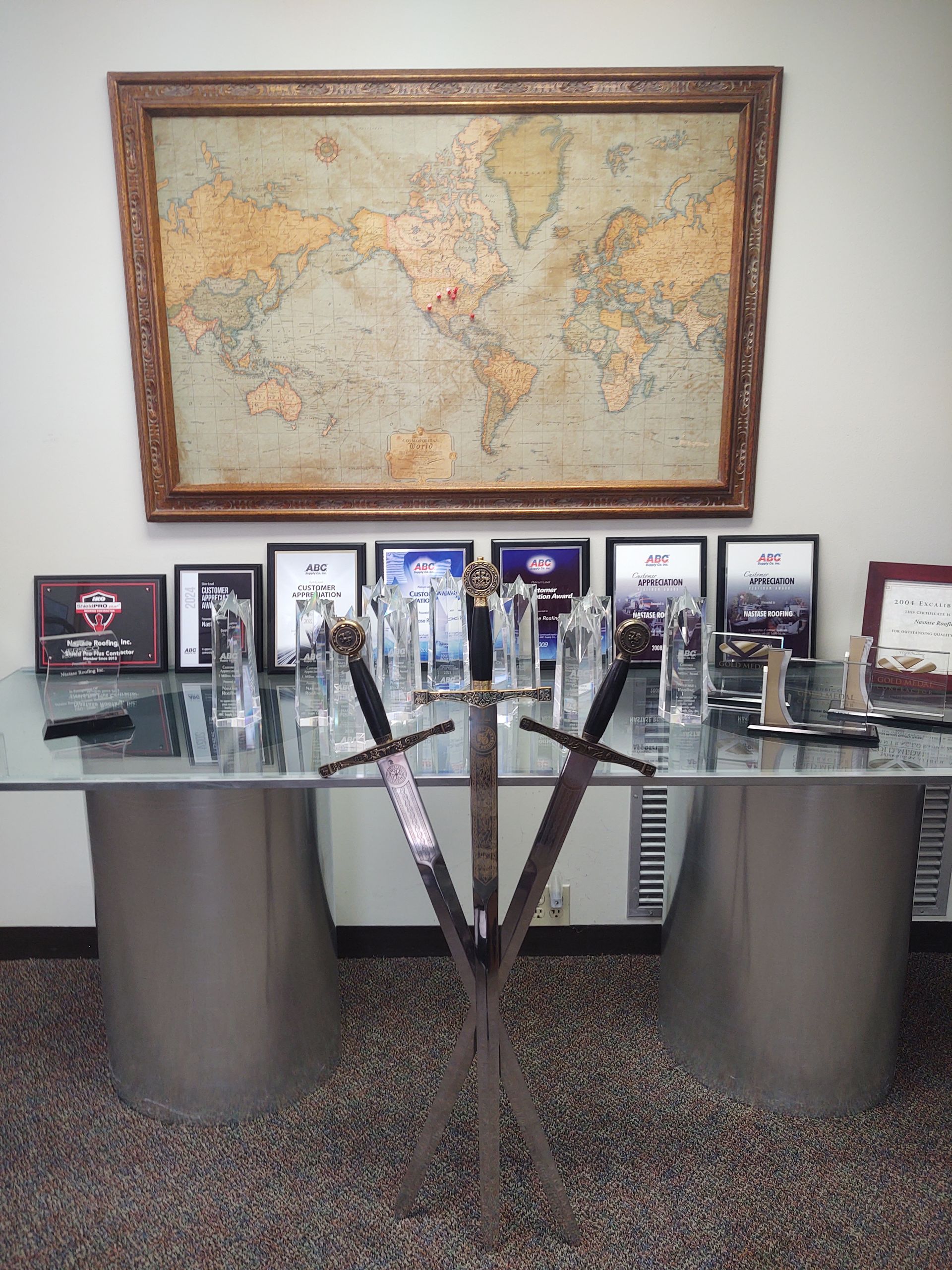 A large world map hangs above a desk featuring several glass trophies and three crossed swords on a stand.