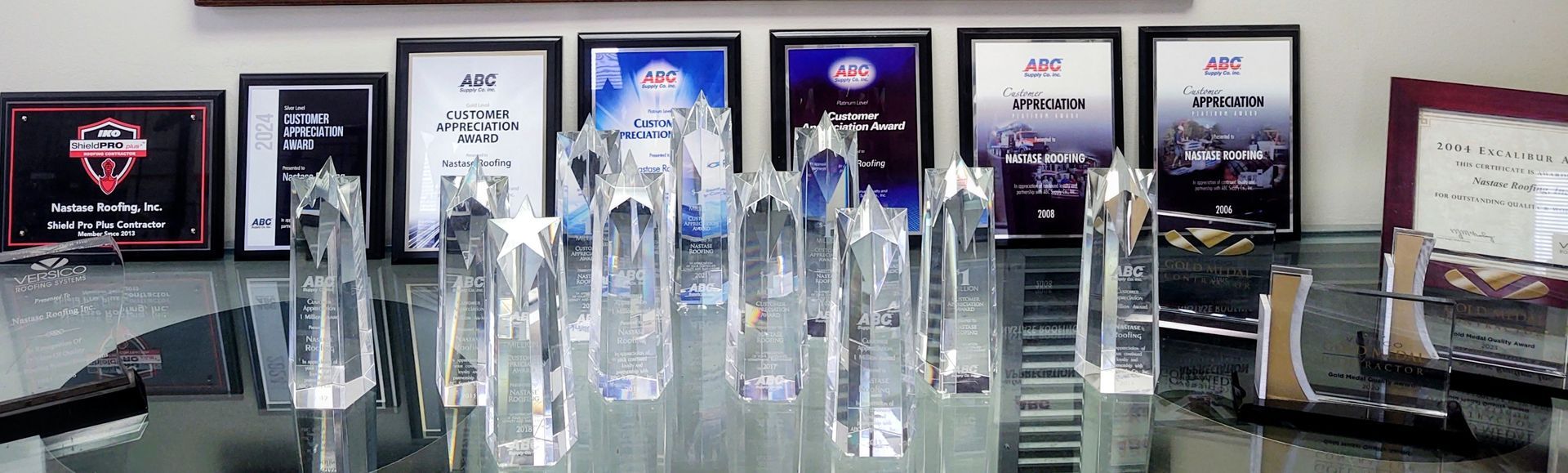 A collection of crystal awards and framed certificates arranged on a glass table in a professional office setting.
