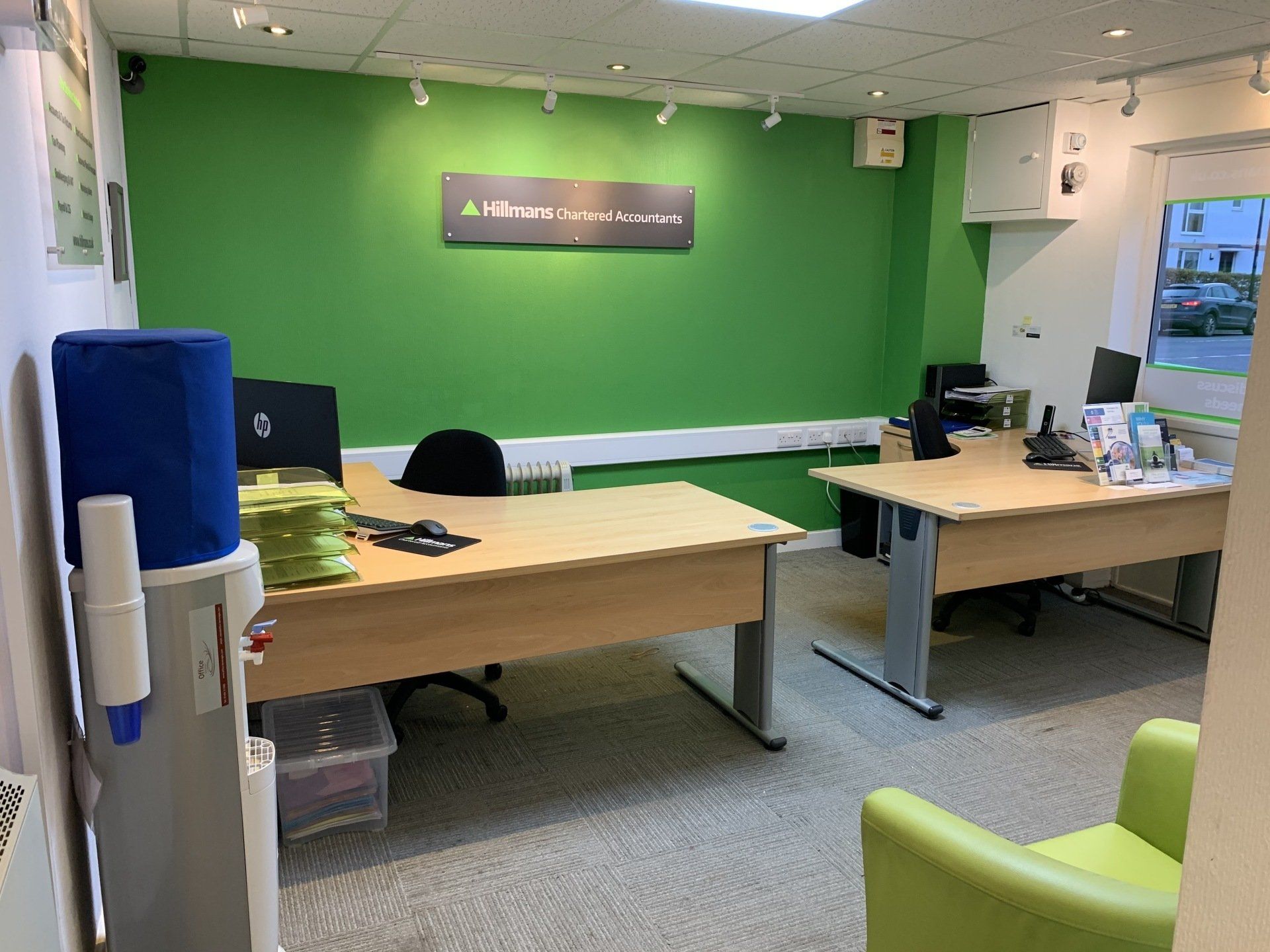 A room with a green wall and wooden desks and chairs.