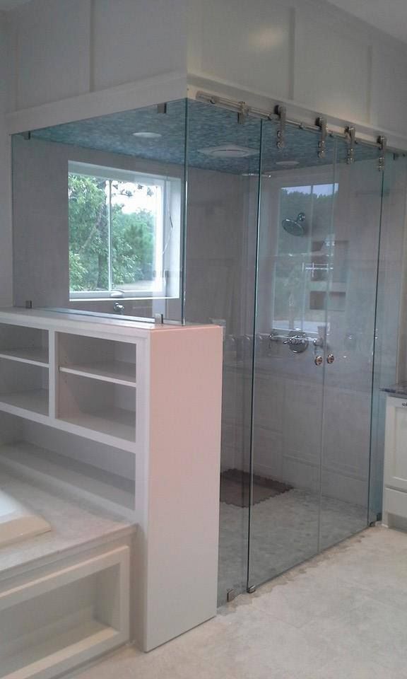 Glass shower enclosure with sliding door, next to a window and built-in storage.