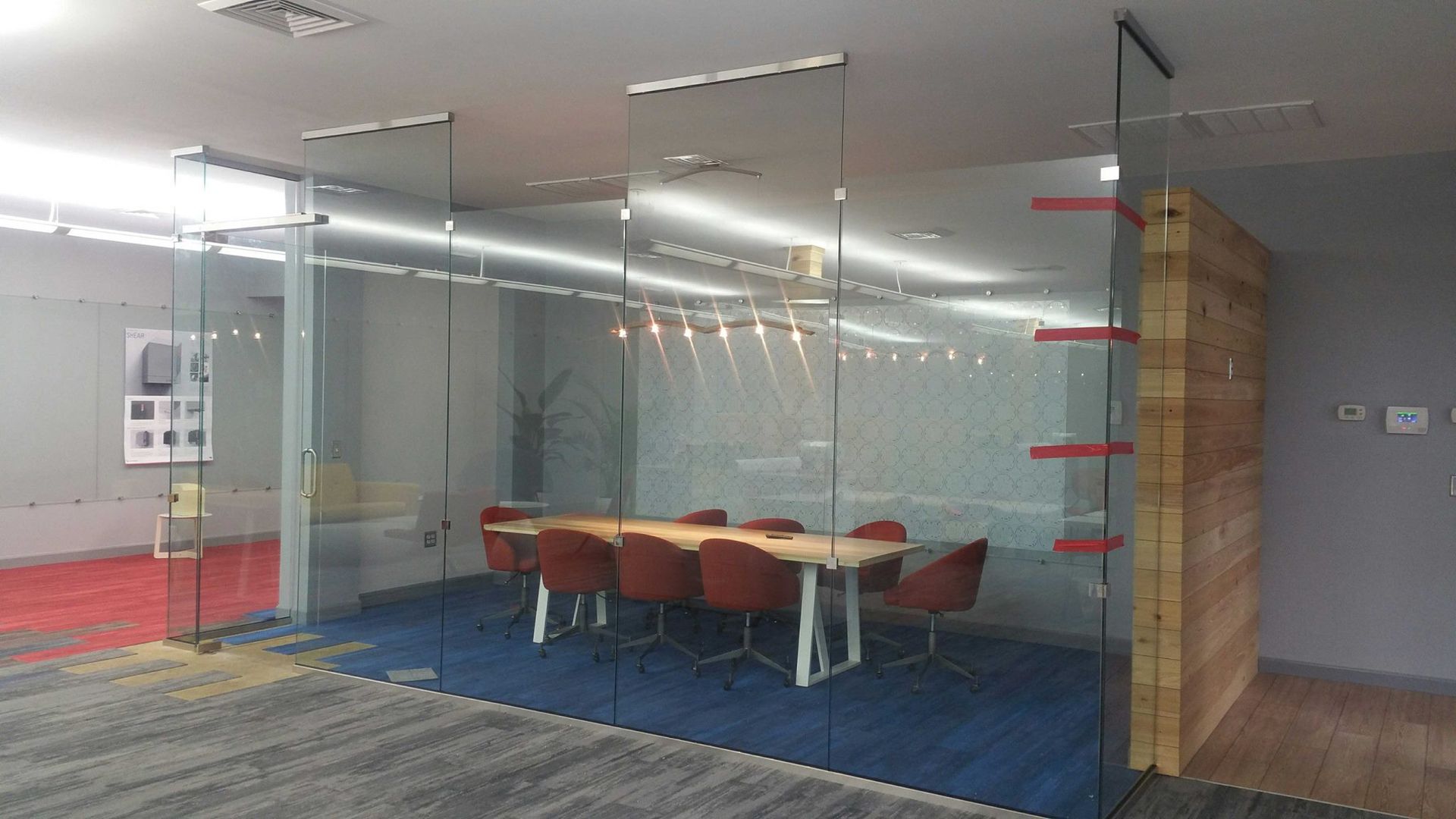 Conference room with glass walls, wooden table and red chairs, blue carpet, and wood panel accent.