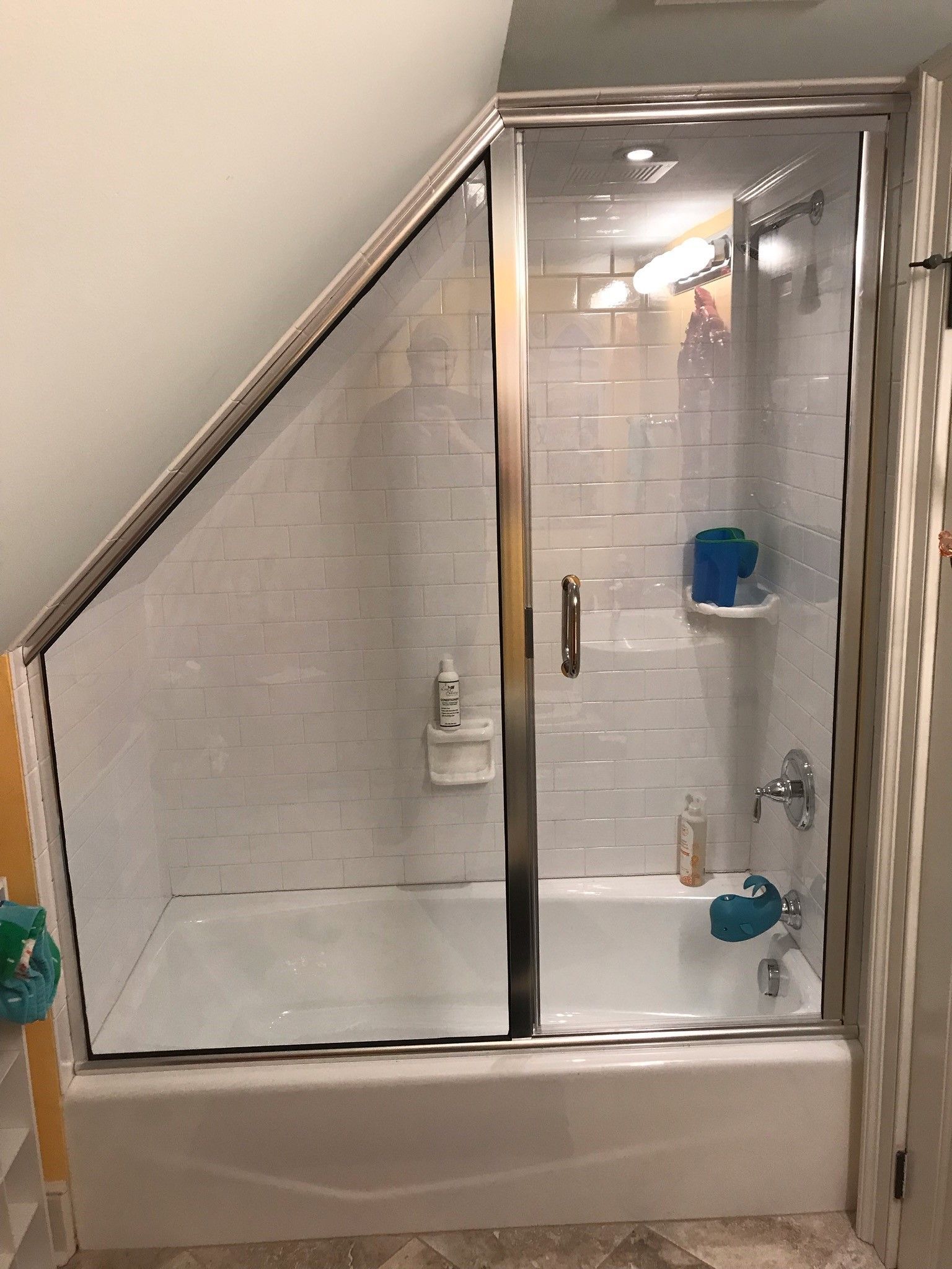 Bathroom shower with angled ceiling, white tile, glass door, and chrome fixtures.