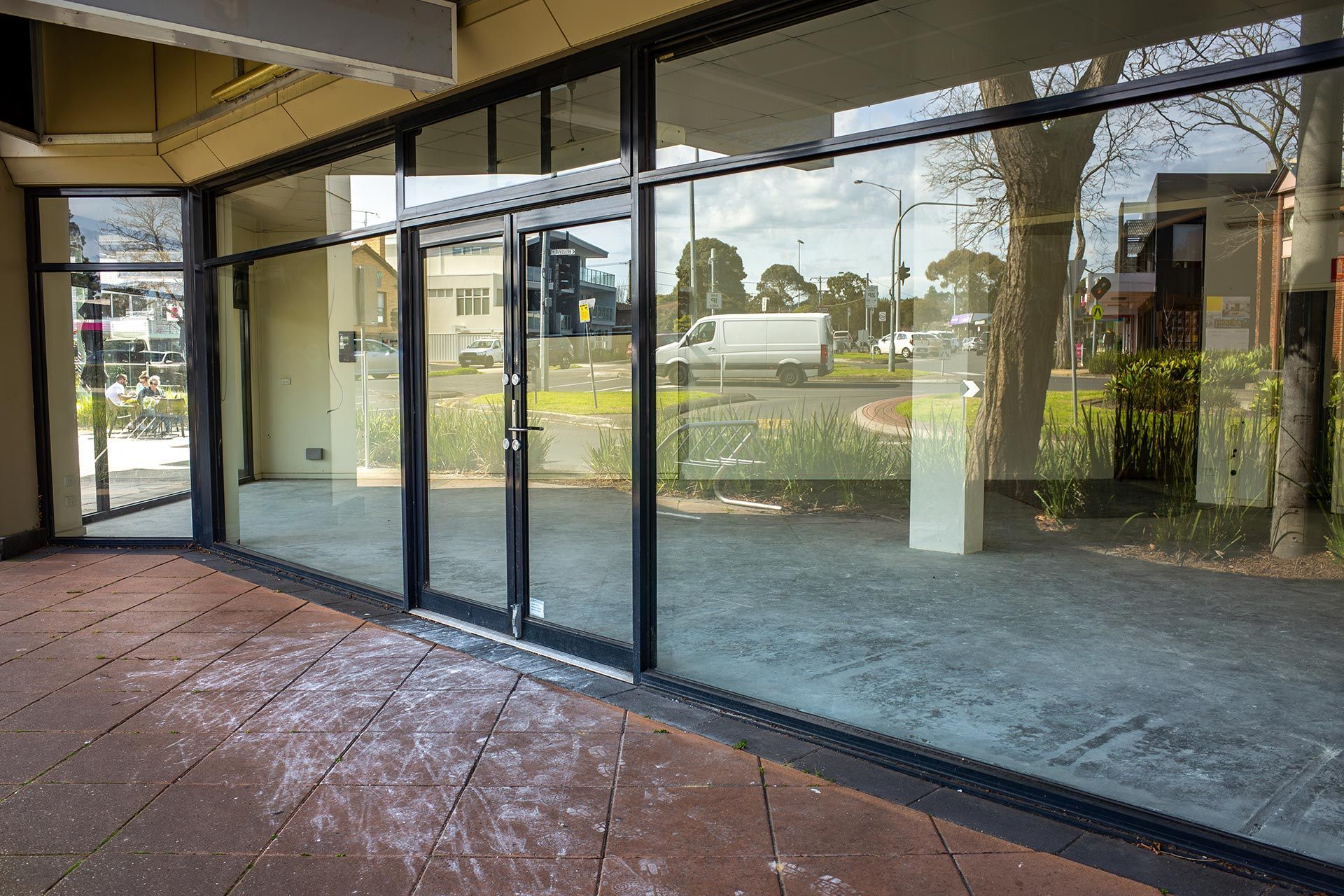 Empty commercial storefront with large glass windows and doors reflecting the corner street view.