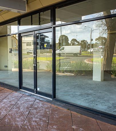 Empty commercial storefront with large glass windows and doors reflecting the corner street view.