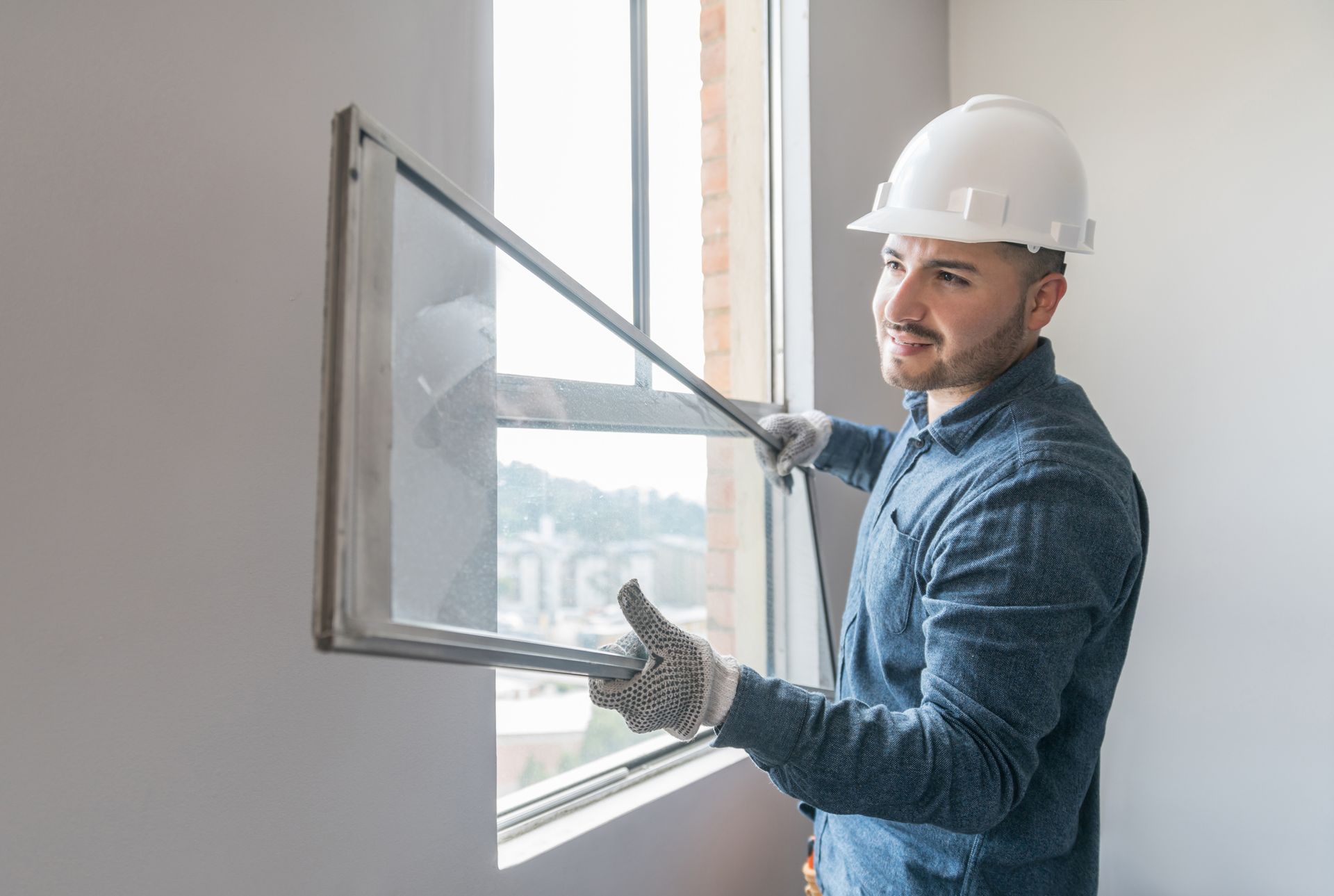 A man in a hard hat holds a window frame, ready for home glass replacement work.