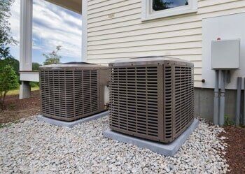 Two air conditioners are sitting outside of a house.