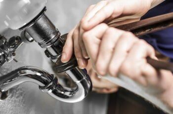 A plumber is fixing a sink pipe with a wrench.