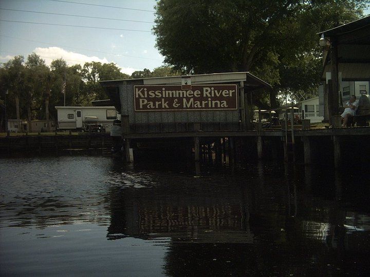 A sign for kissimmee river park and marina is above a body of water