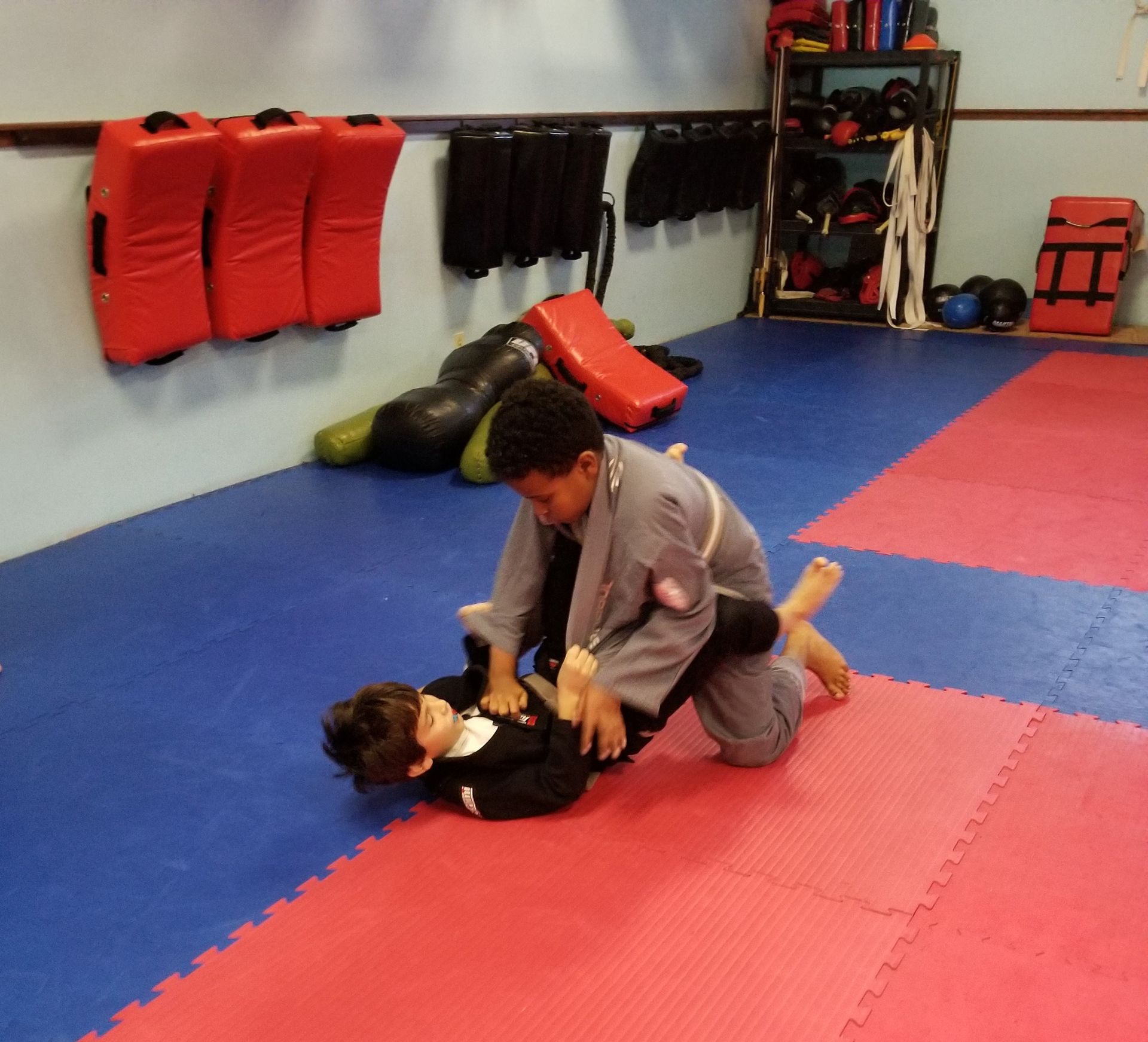 two boys are wrestling with one wearing a black karate uniform with the word jiu-jitsu on it