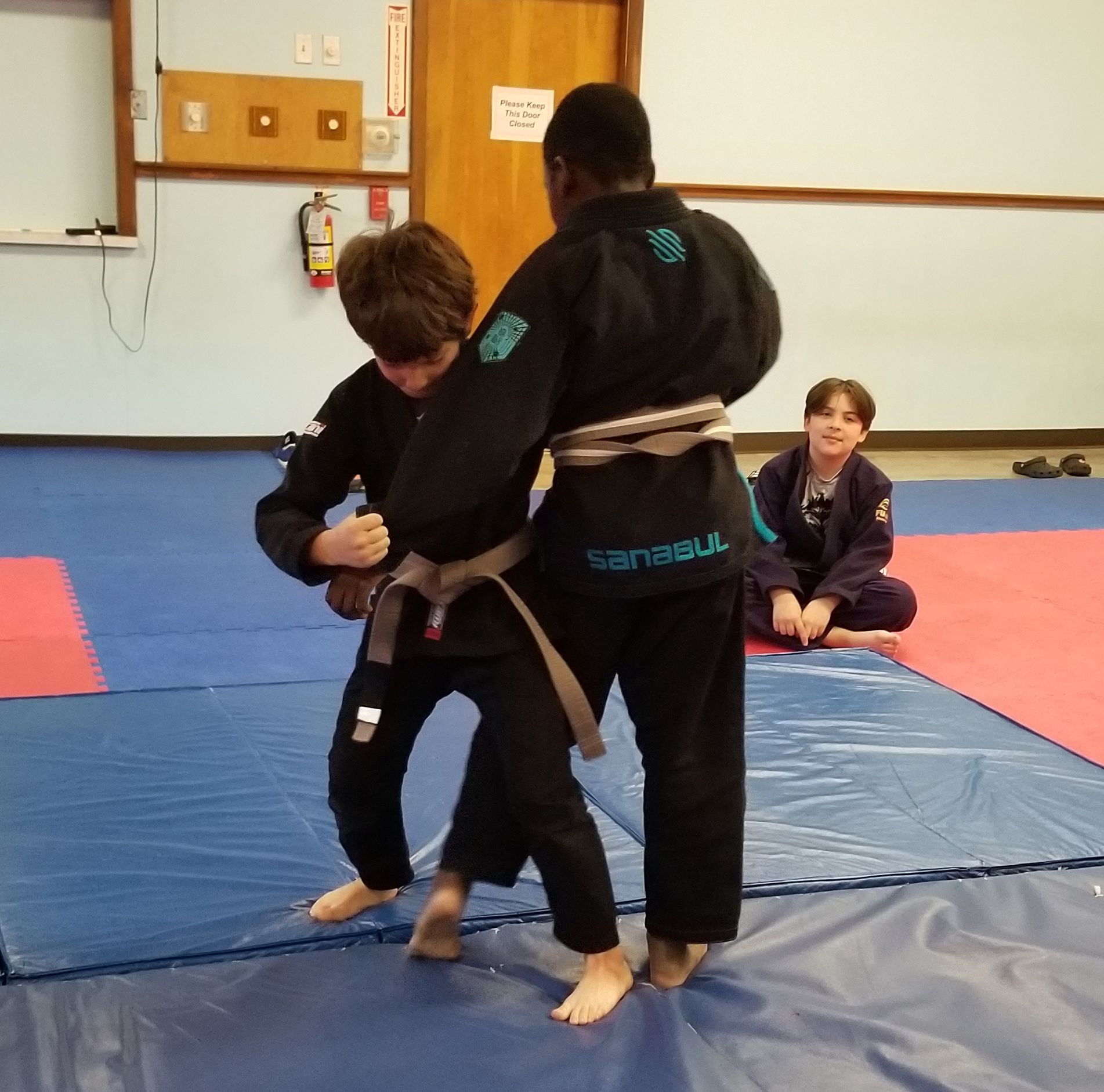 Two young boys are practicing judo in a dark room.