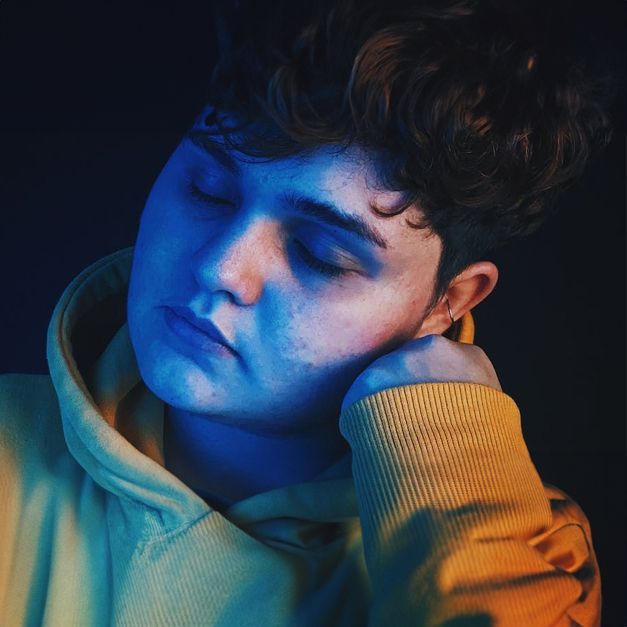 a young man in a yellow hoodie is sleeping with his eyes closed .