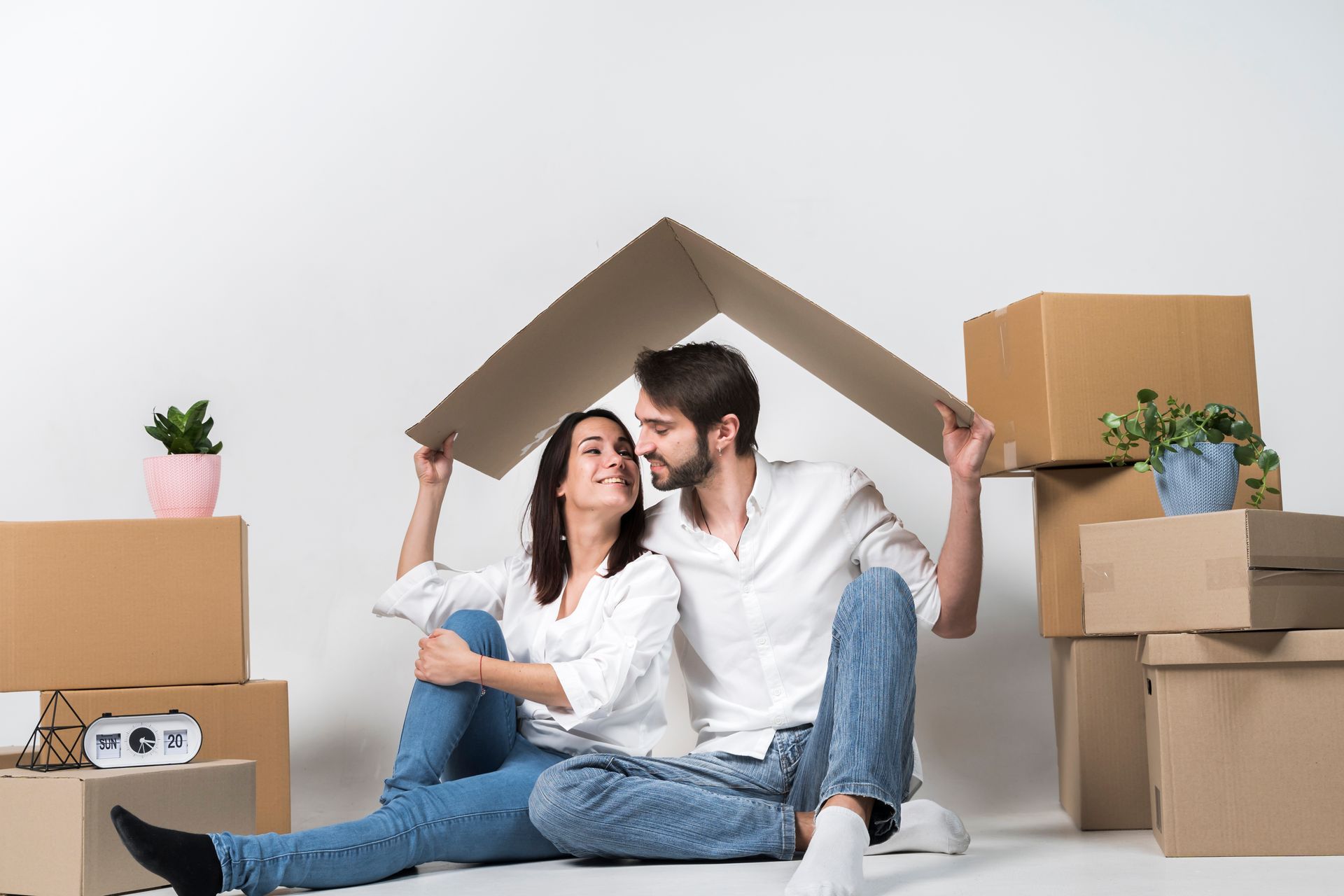 Couple under cardboard house roof with moving boxes.