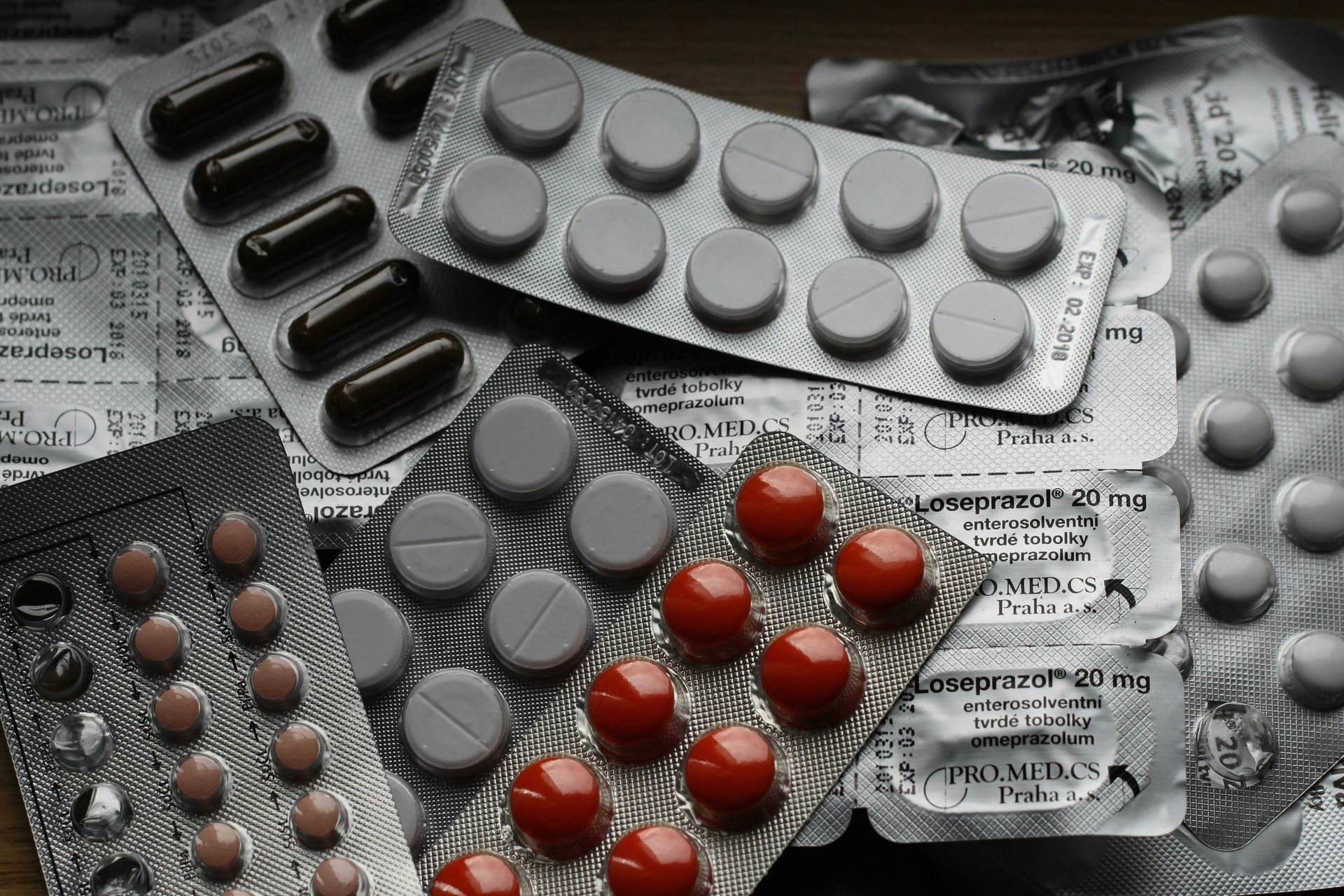 Various blister packs of pills, including red, brown, and white tablets, on a surface.