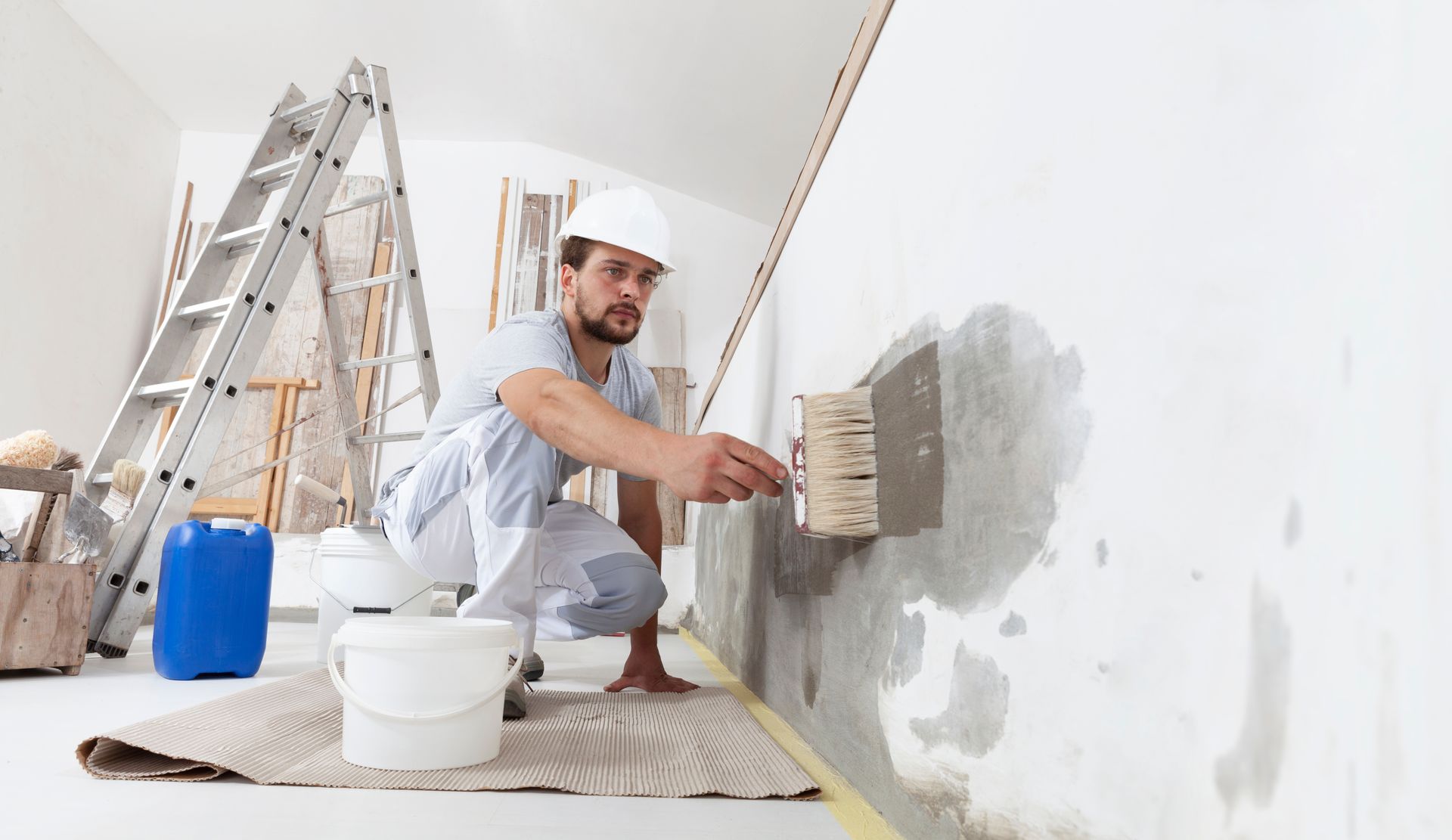 A man is kneeling down and painting a wall with a brush.