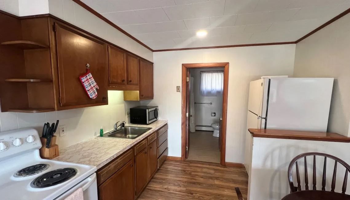 A kitchen with a stove , refrigerator , sink and chair.