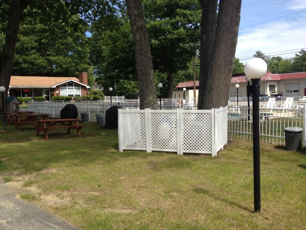 A white fence surrounds a picnic area with a house in the background