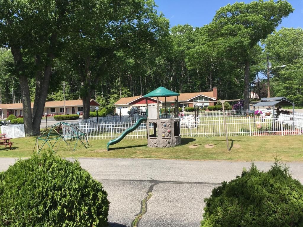 A playground with a slide and umbrella in front of a house.