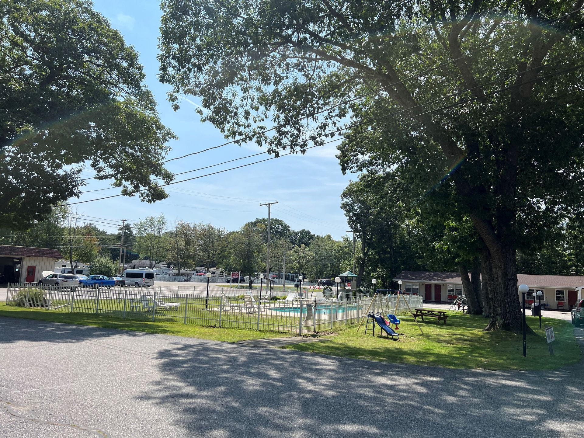 A parking lot with trees and a swimming pool in the background.