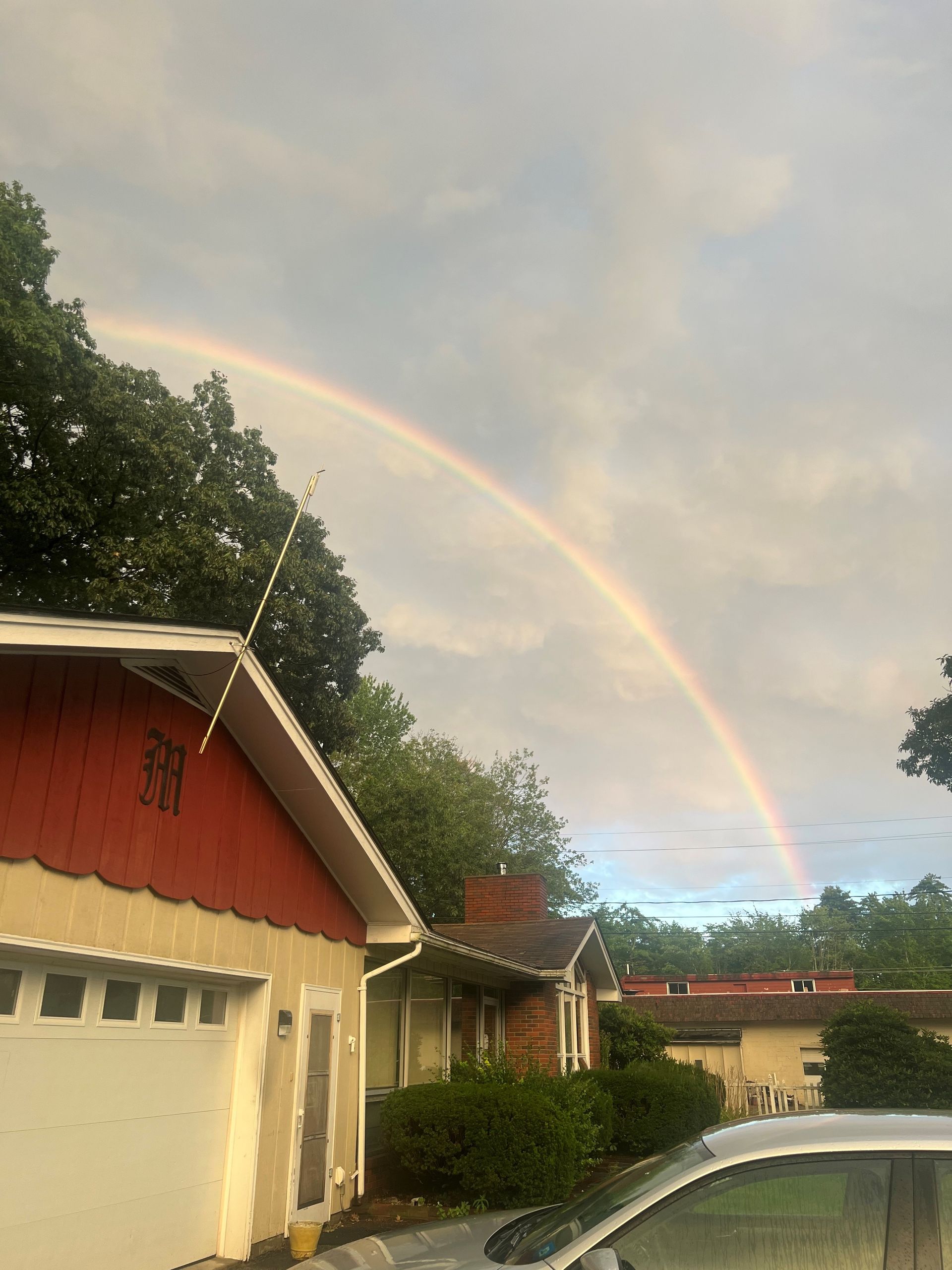 A car is parked in front of a house with a rainbow in the sky