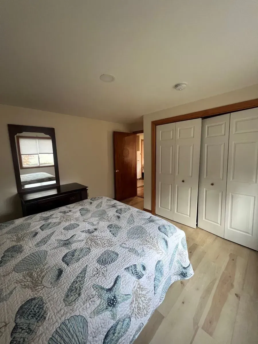 A bedroom with a bed , dresser , mirror and closet.