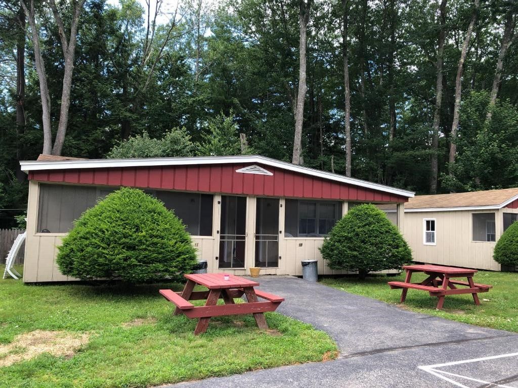A mobile home with a red roof and two picnic tables in front of it.