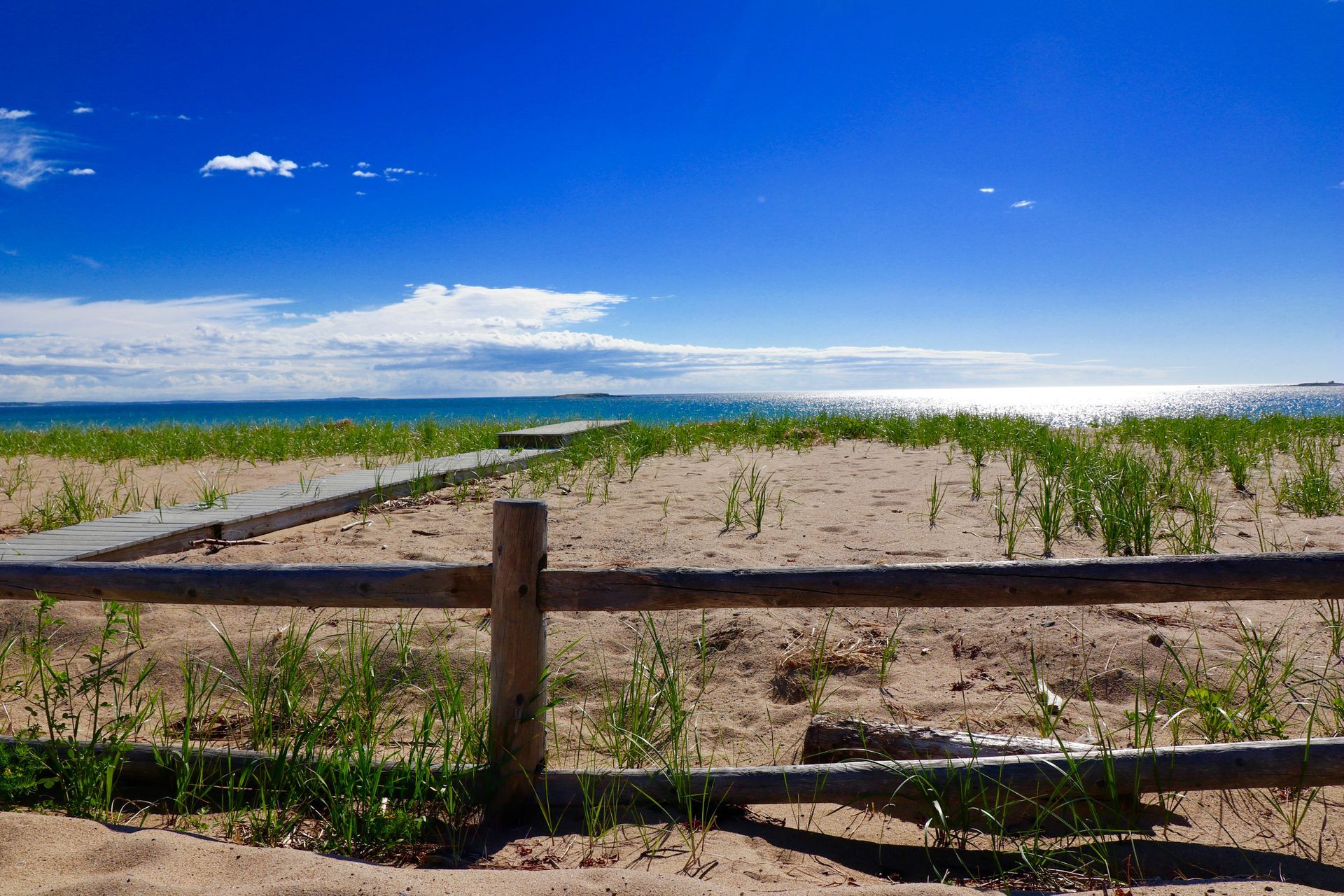 A wooden fence surrounds a sandy beach with a view of the ocean.