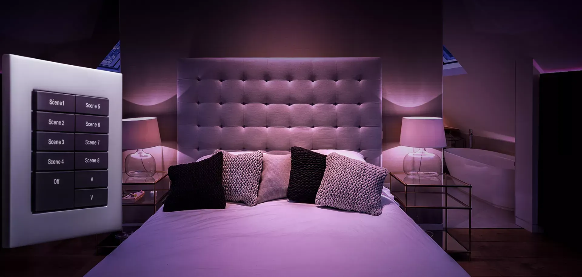 Bedroom with purple lighting, tufted headboard, pillows on bed, and wall-mounted control panel.