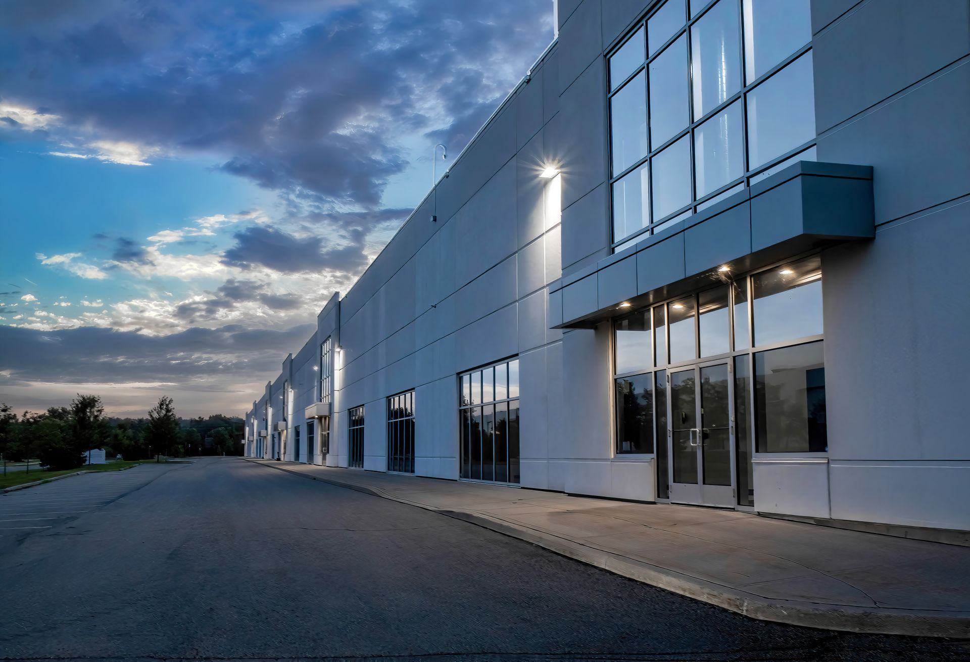 Exterior of a modern industrial building with large windows, under a twilight sky.