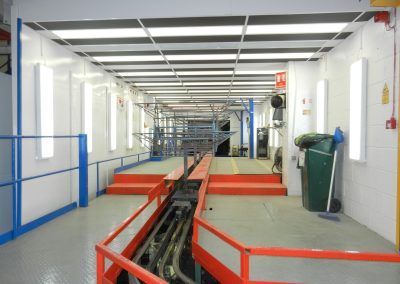 Long industrial hallway with red and blue accents, overhead lighting, and equipment visible in the distance.