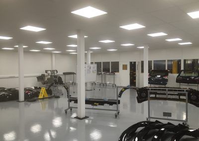 A bright, white automotive workshop with car parts, tools, and several support pillars.