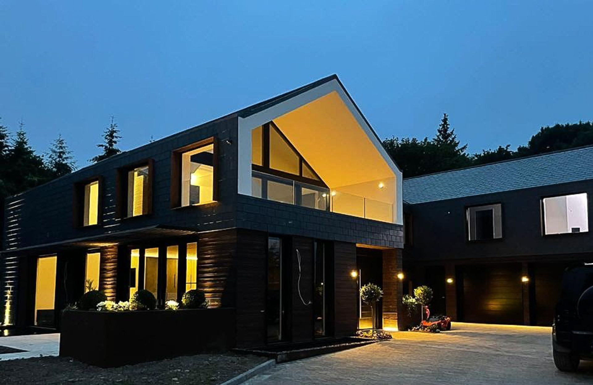 Modern black house with lit windows and open balcony, set against a twilight sky.