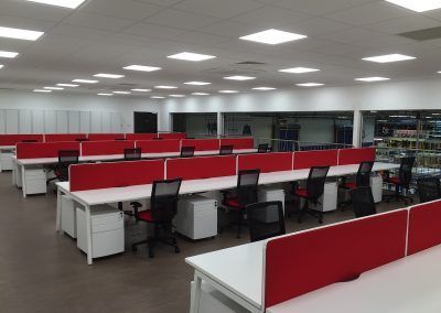 Rows of white desks with red dividers in an open office space, black mesh chairs, and white storage cabinets.