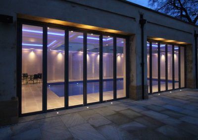Indoor pool with large glass folding doors, lit with blue and white lights.